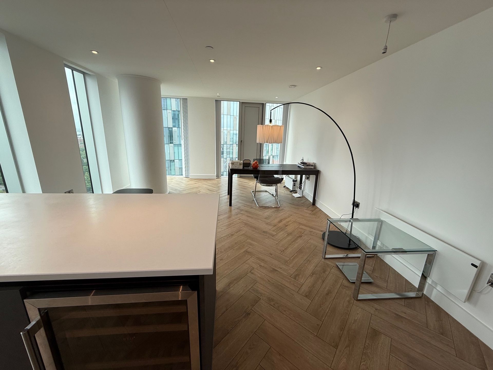 Modern apartment interior with a desk, floor lamp, and a kitchen island.