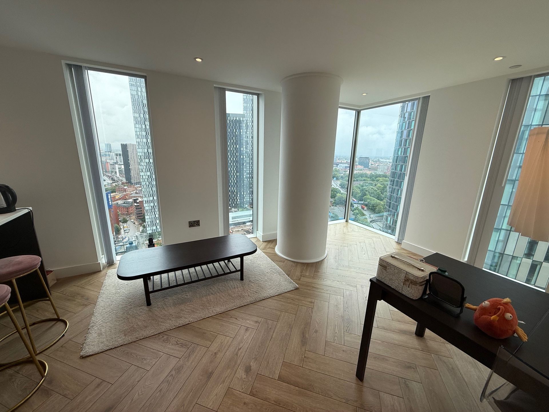 Modern apartment interior with city views, featuring a table, rug, and large windows.