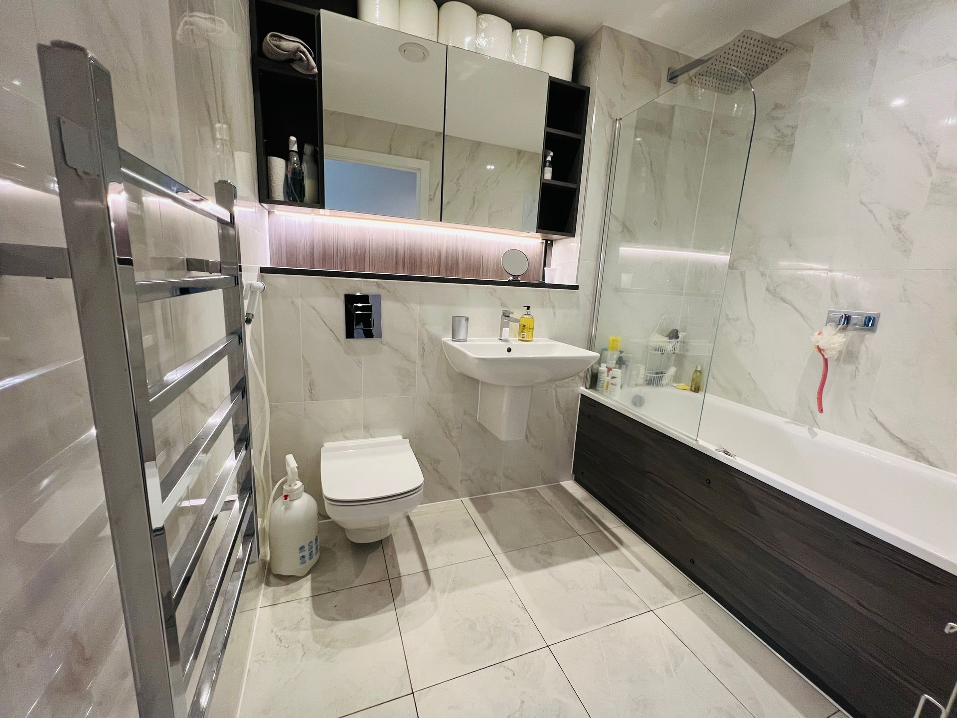 Modern bathroom with white and gray tiled walls, toilet, sink, tub, and heated towel rack.