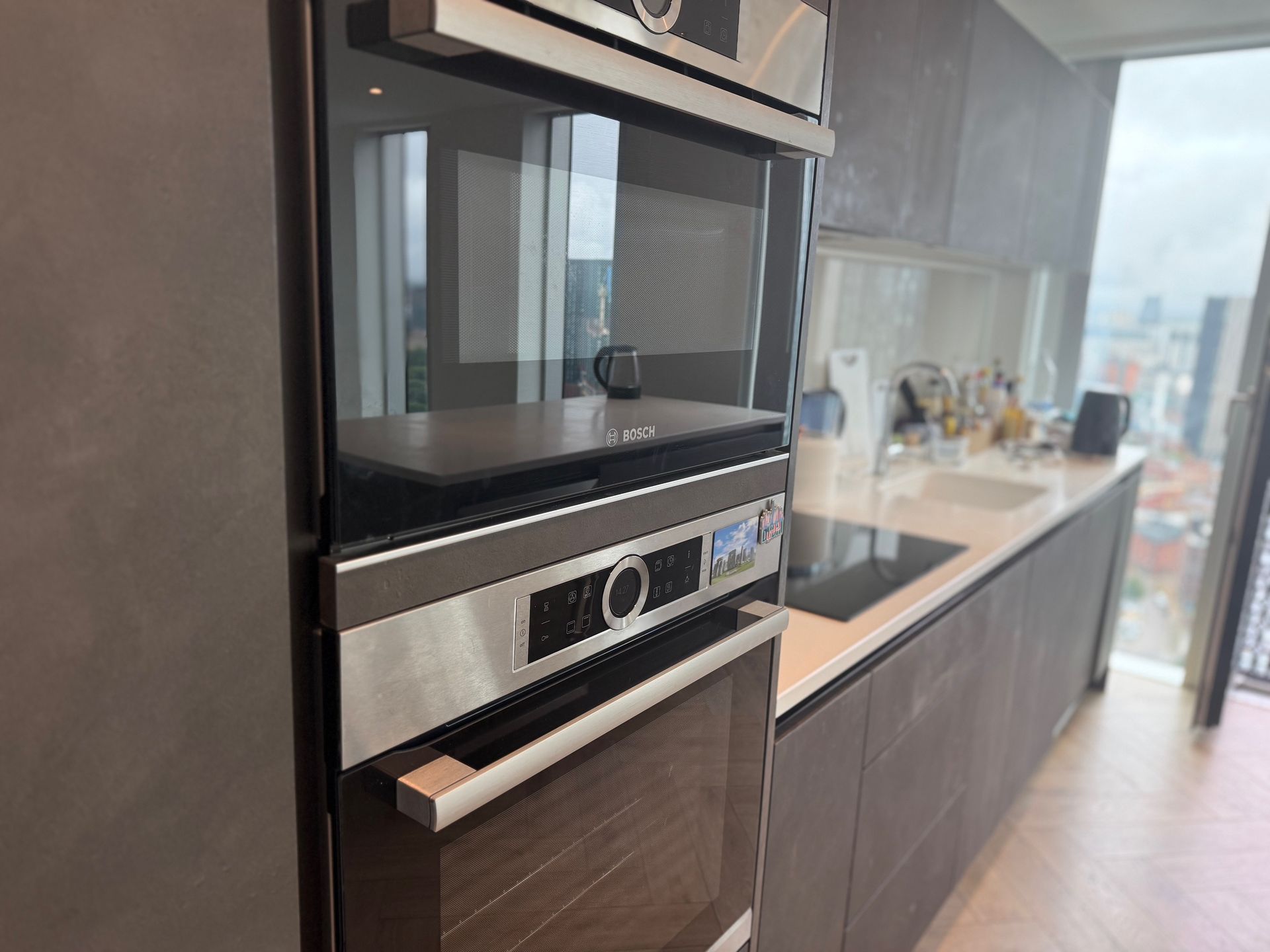 Built-in stainless steel oven and microwave in modern kitchen with city view.