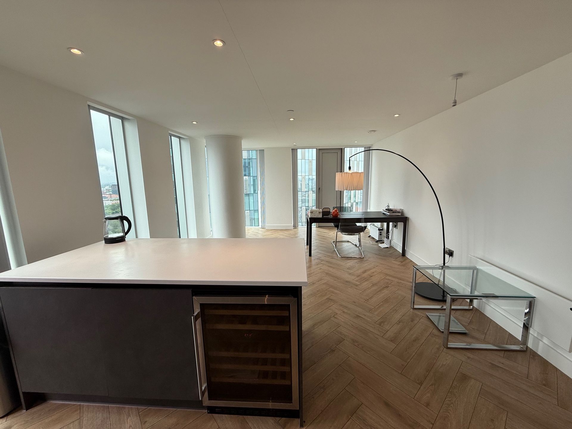 Modern apartment interior with kitchen island, desk, and large windows with city view.