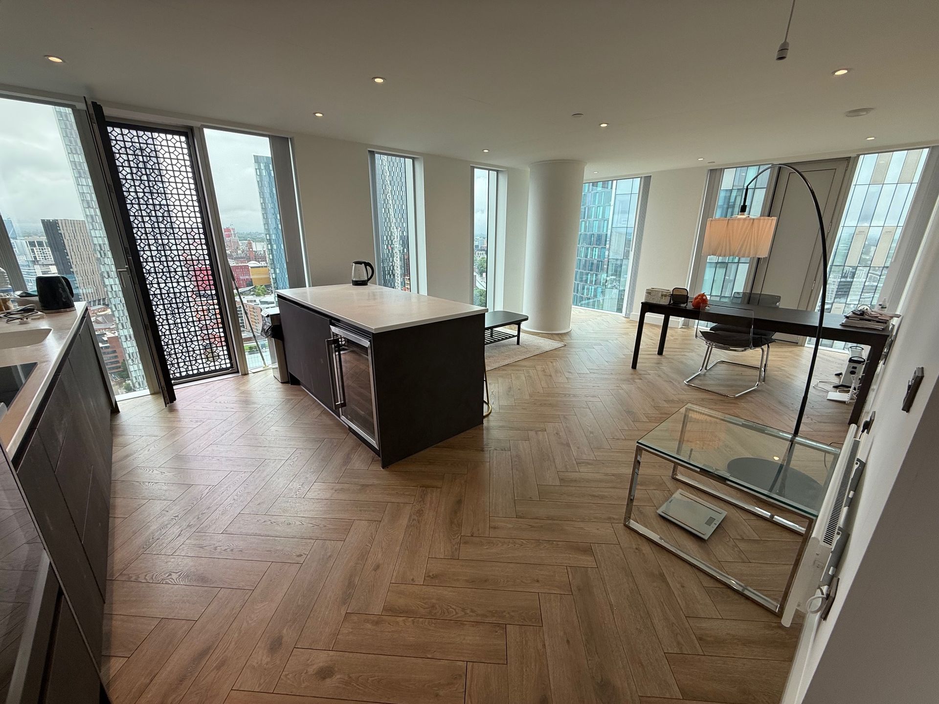 High-angle view of a modern apartment interior with city views, hardwood floors, and kitchen island.