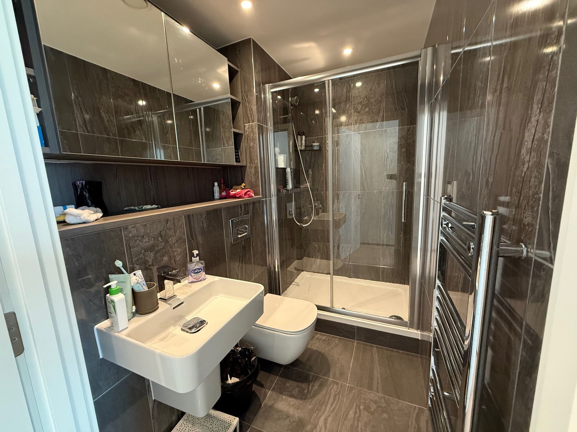 Modern bathroom with gray marble walls and flooring, a glass shower, and a floating sink.