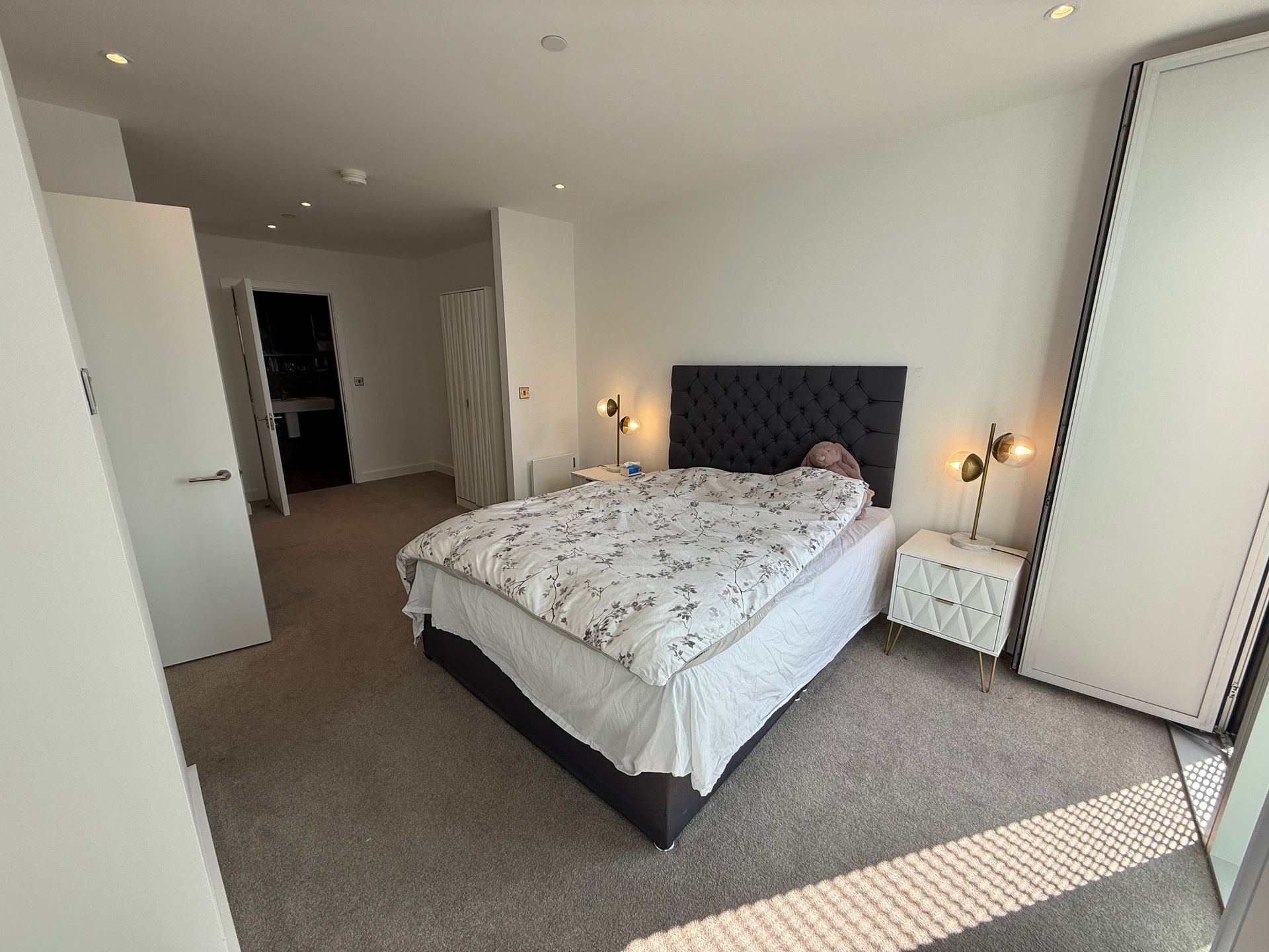Bedroom with bed, nightstands, open door to bathroom, and large window.