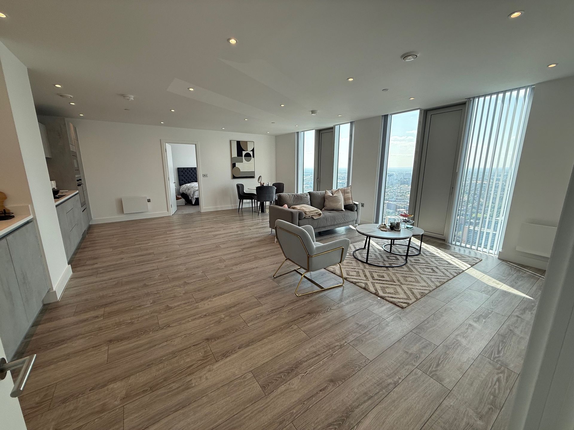 Spacious modern apartment with wooden floors, living area with sofa, and large windows.