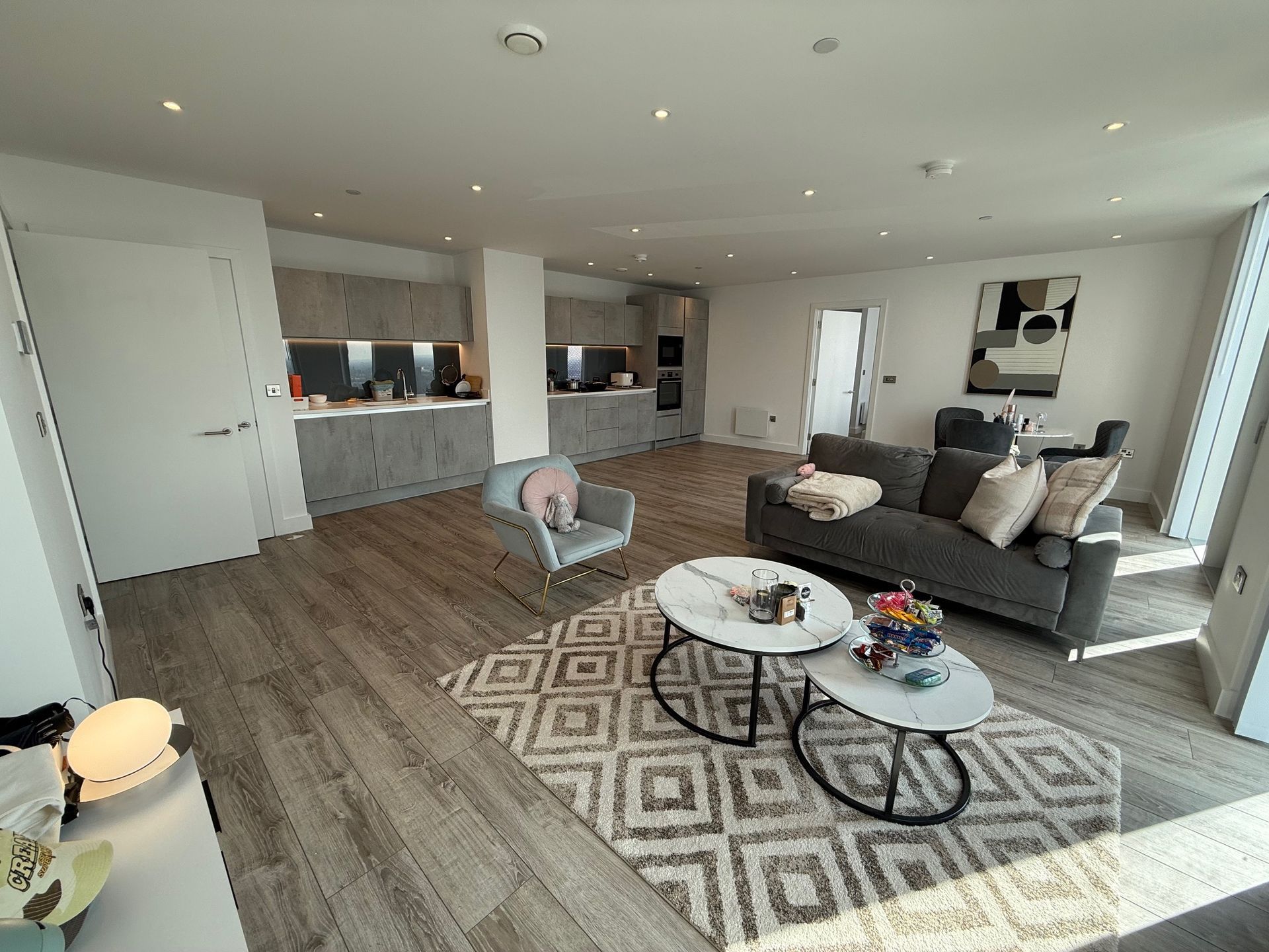 Modern living room with open kitchen, gray sofa, area rug, and artwork.