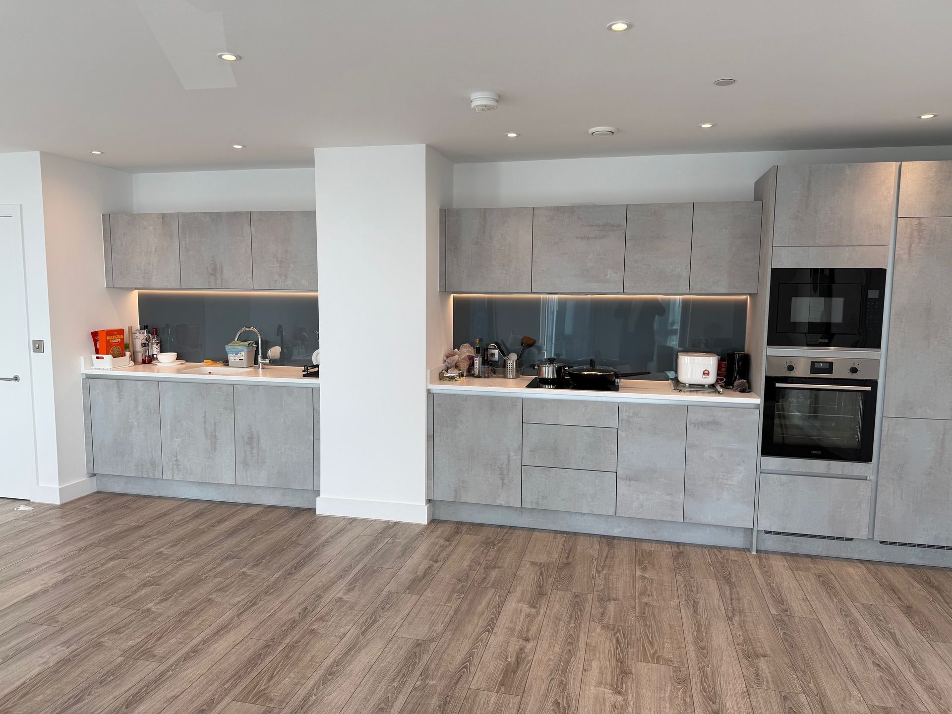 Modern kitchen with gray cabinets, wood-look flooring, built-in appliances, and a central white column.