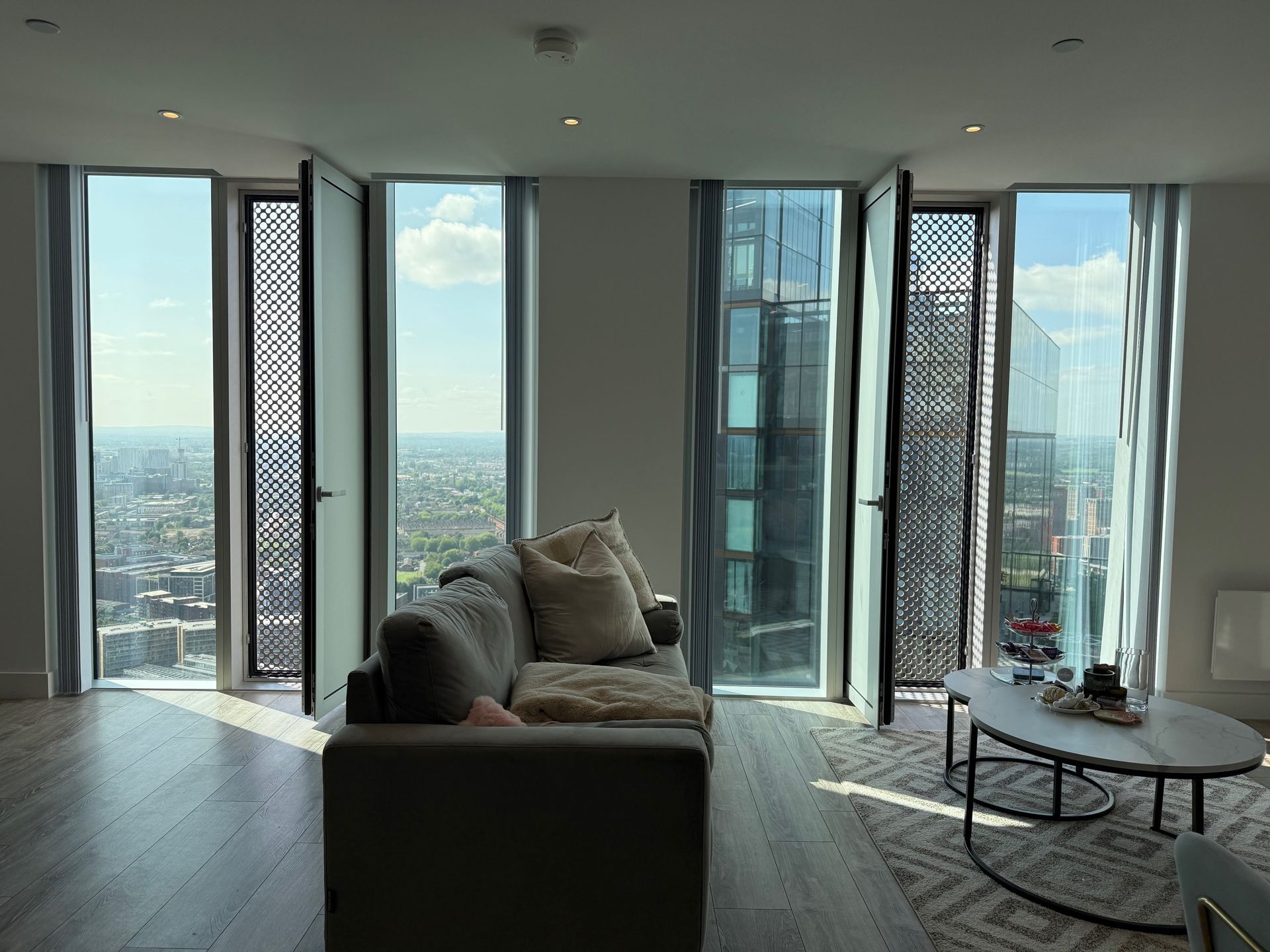 Living room with large windows, city view, gray sofa, coffee table, and patterned rug.
