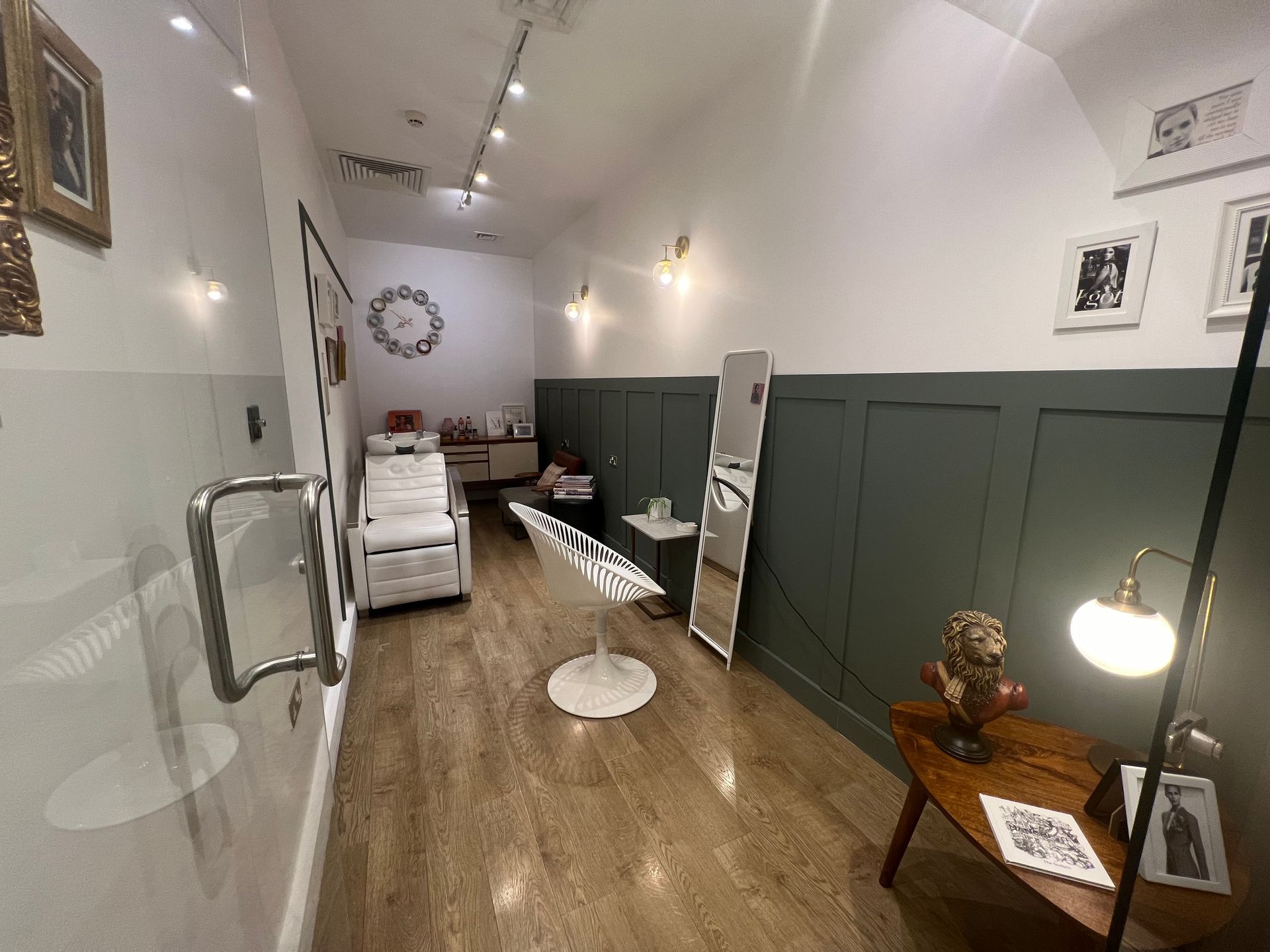 Small beauty treatment room with white and green walls, bed, chair, mirror, and decorative items.