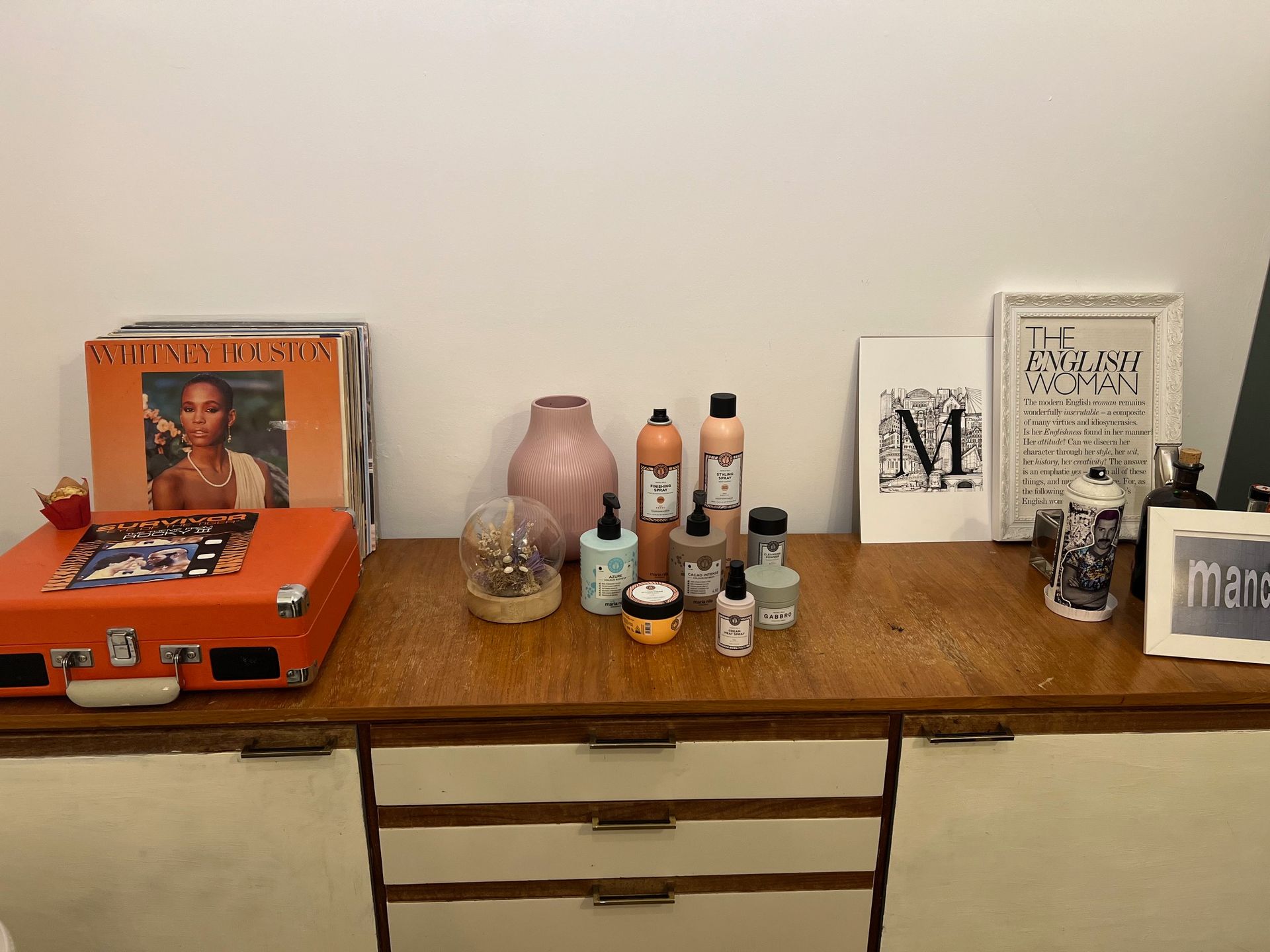 A wooden table with a record player, bottles, vases, and framed art against a white wall.
