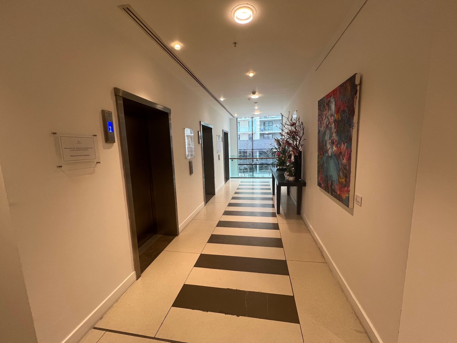 Hallway with elevators, black and white striped floor, artwork, and a table with flowers.