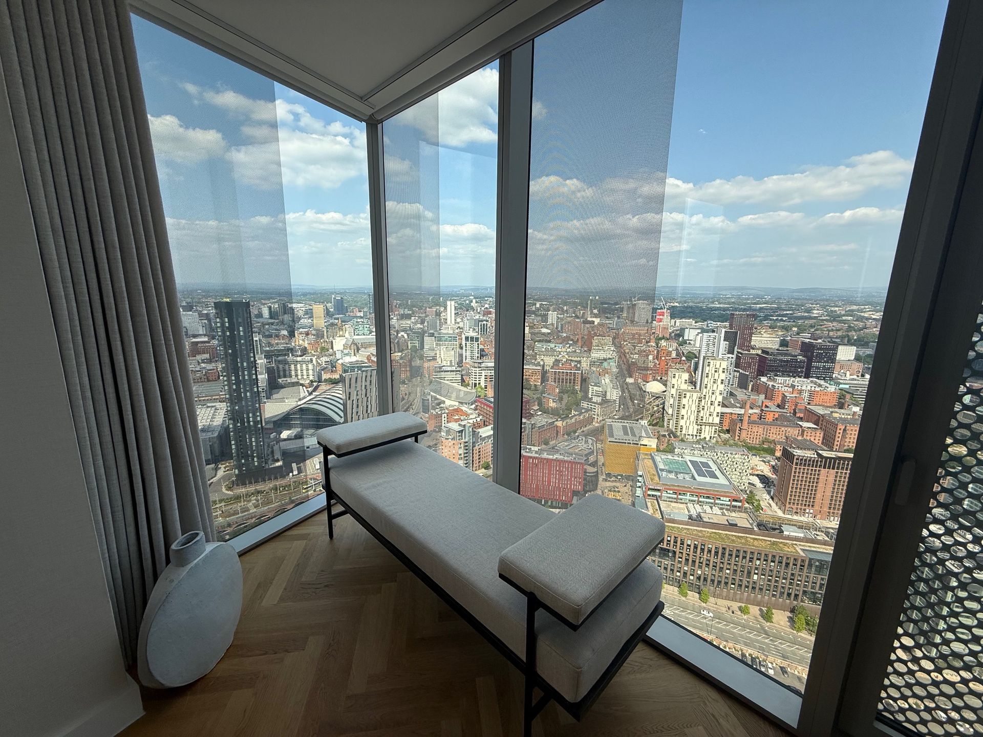 A modern chaise lounge sits by a large window with a panoramic city view.