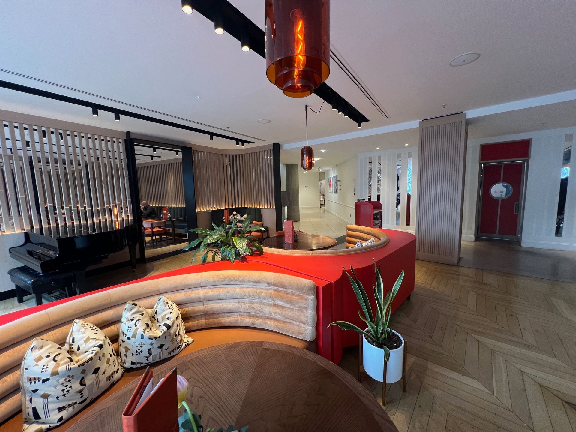 Lounge area with a curved red sofa, piano, and amber pendant lights.