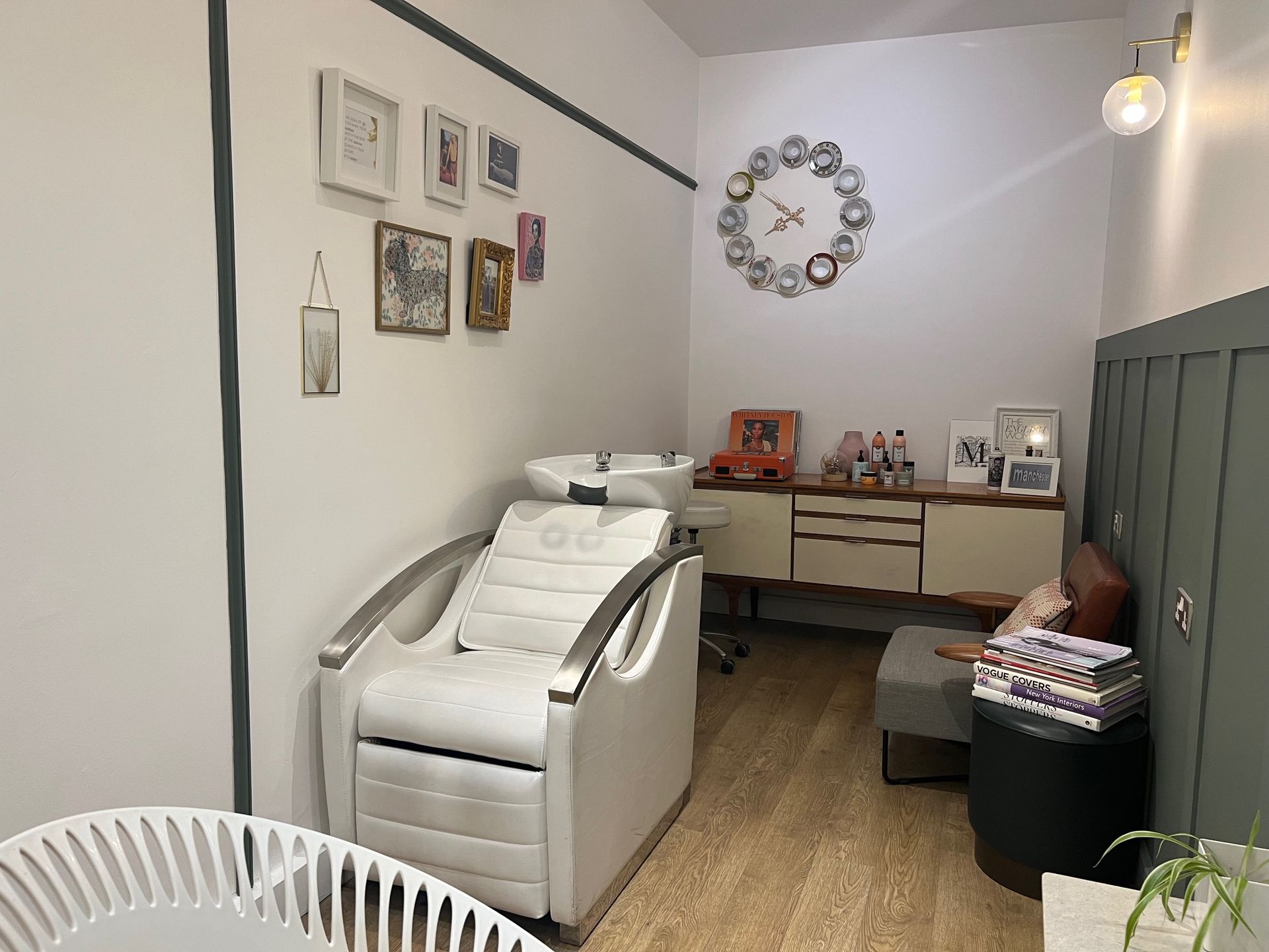 Salon interior with a hair-washing chair, sink, artwork, and a clock.