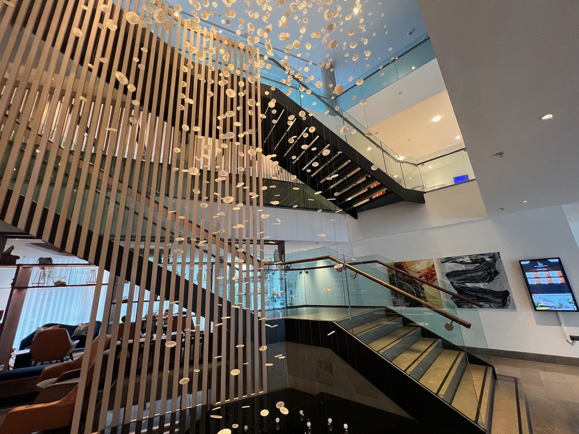 Interior view of a modern staircase. Wooden slat wall with overhead chandelier.