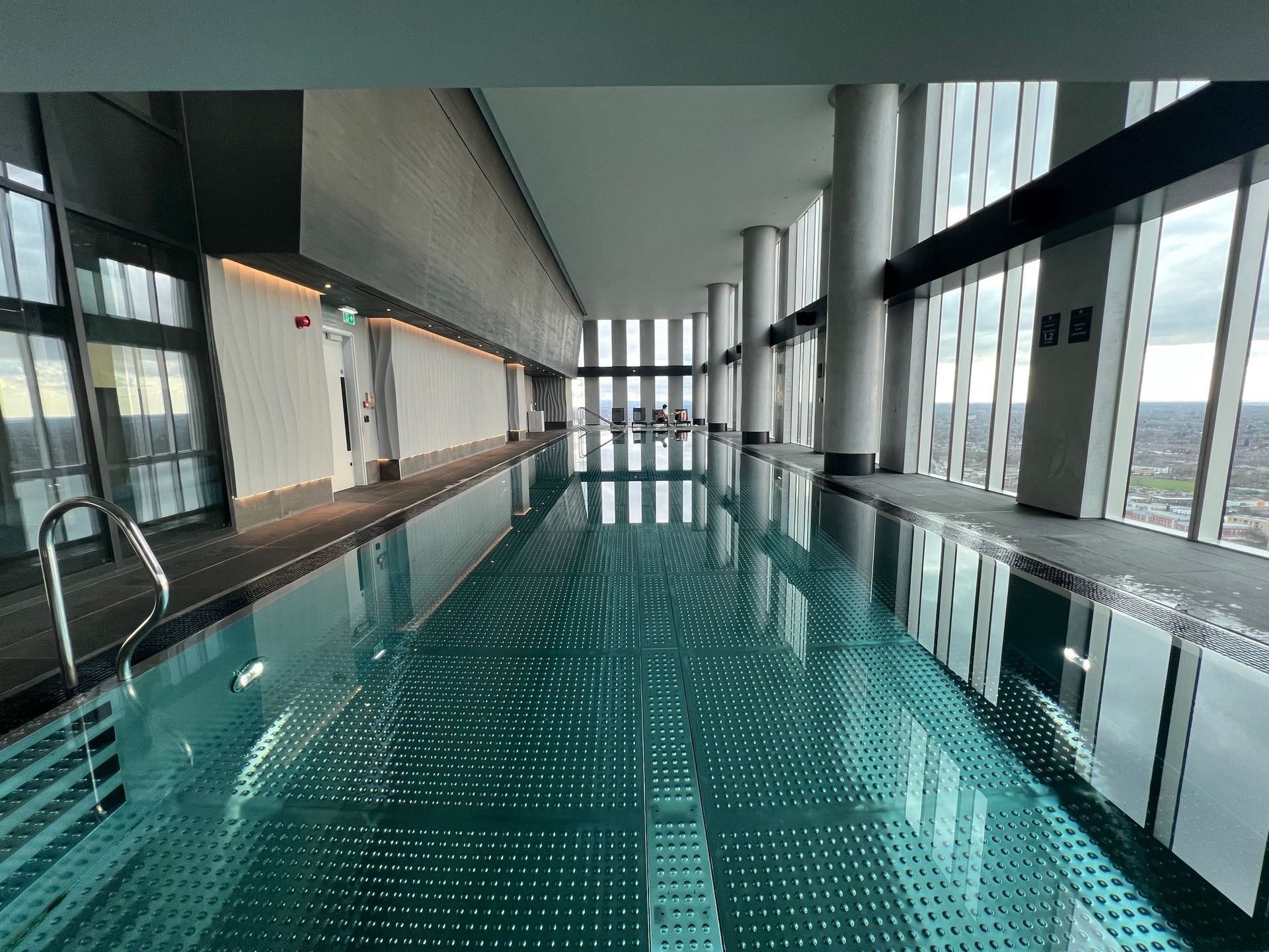 Indoor pool with panoramic city views, floor-to-ceiling windows, and reflective water.