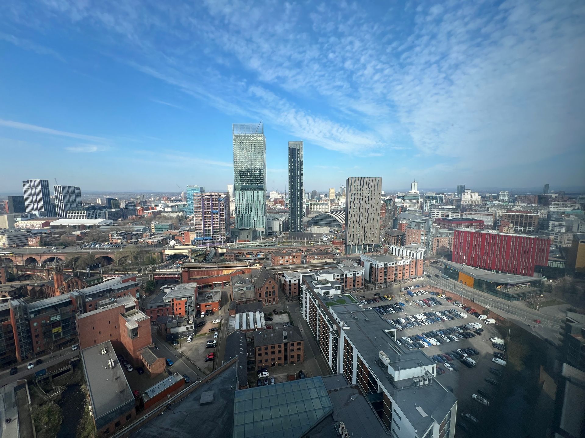 Aerial view of Manchester city skyline on a bright, sunny day. Skyscrapers, buildings, and roads visible.