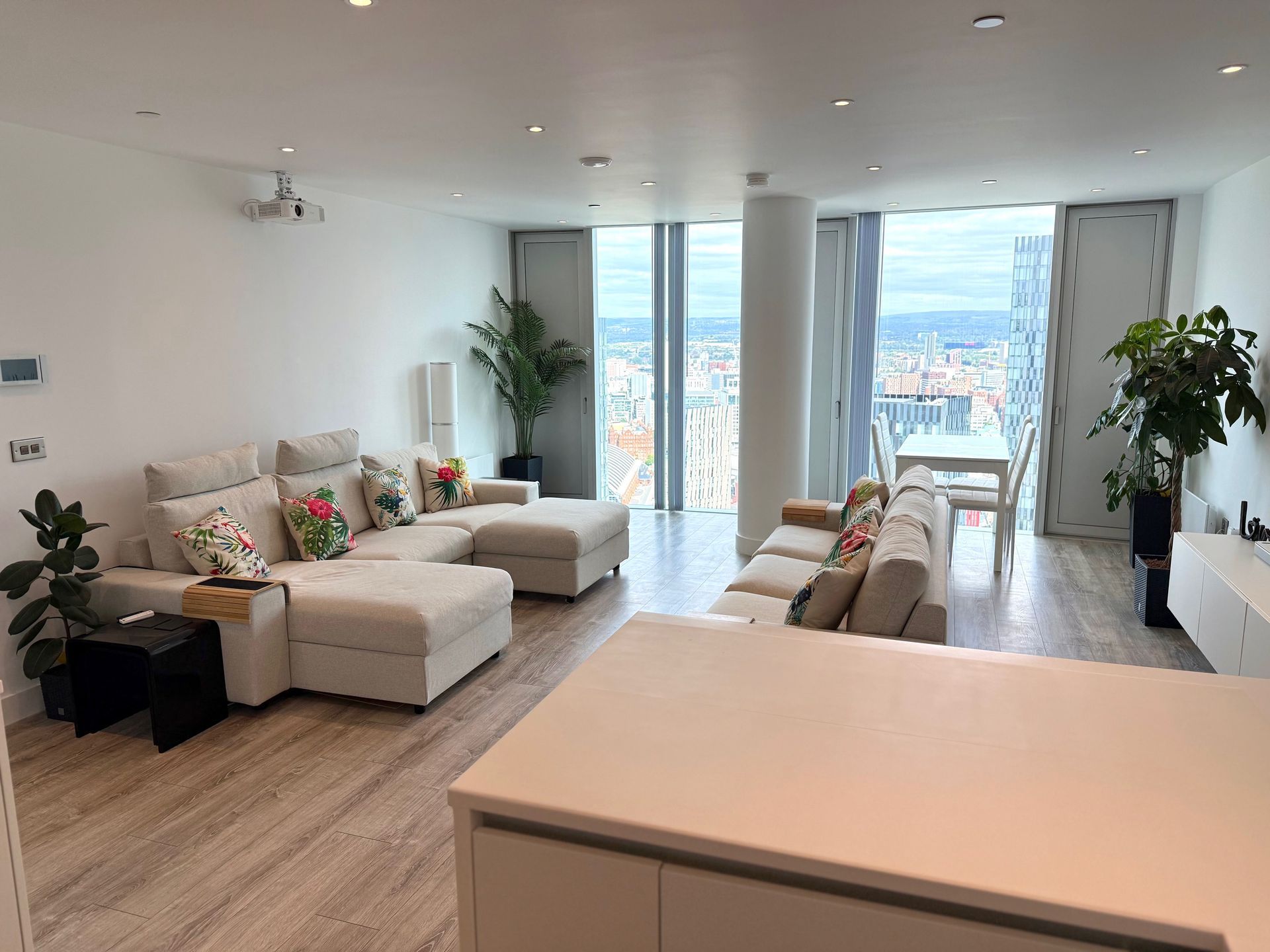 Modern, spacious living room with sectional sofas, city views, and plants.