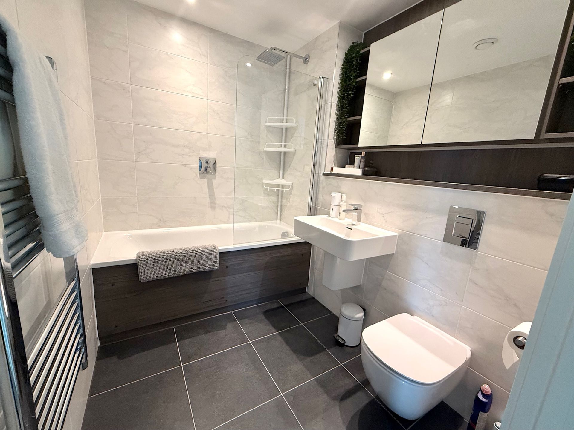 Modern bathroom with a bathtub, shower, toilet, sink, and mirror. Gray and white color scheme.
