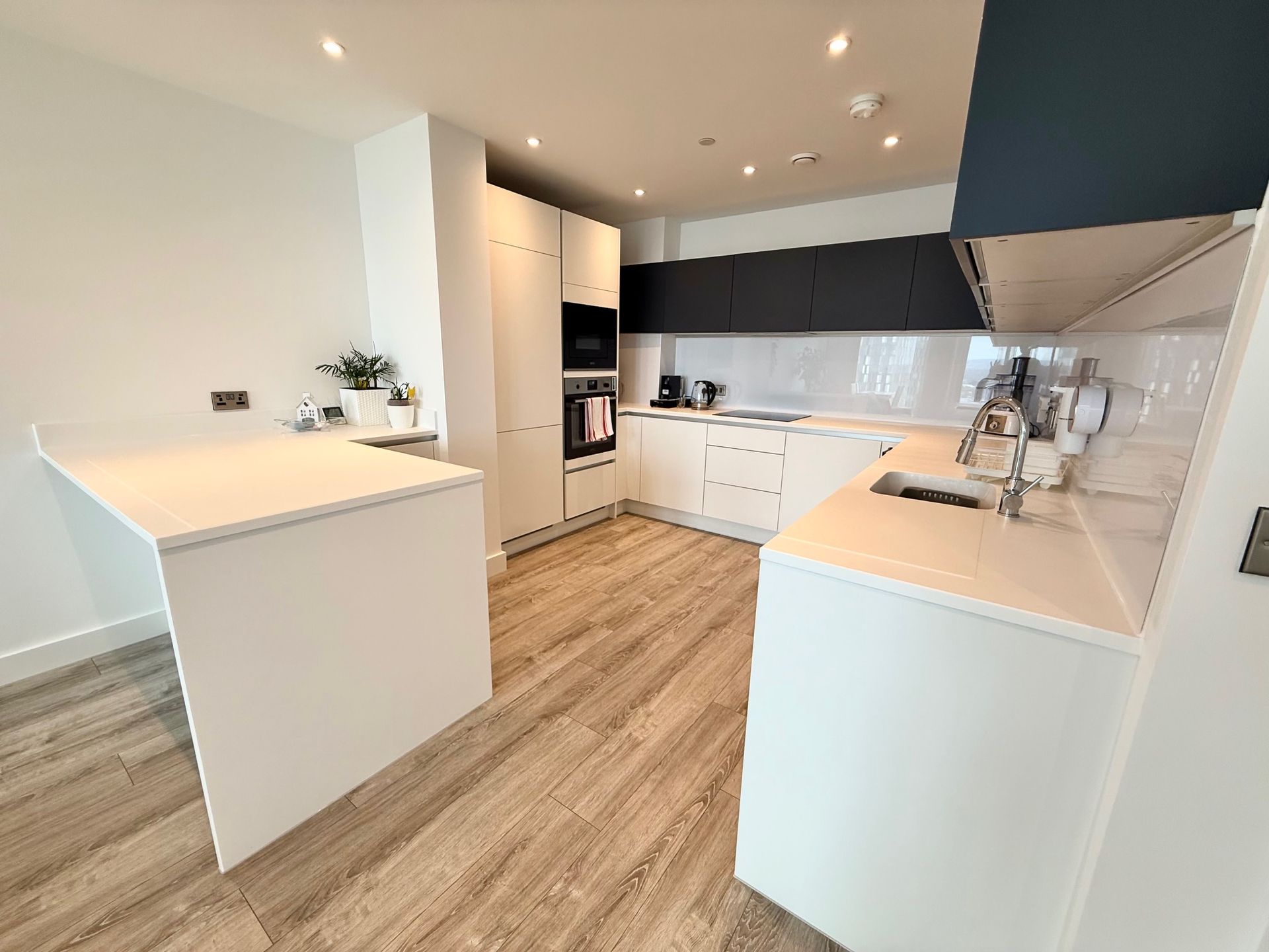 Modern white kitchen with light wood floor, countertop bar, and stainless steel sink.