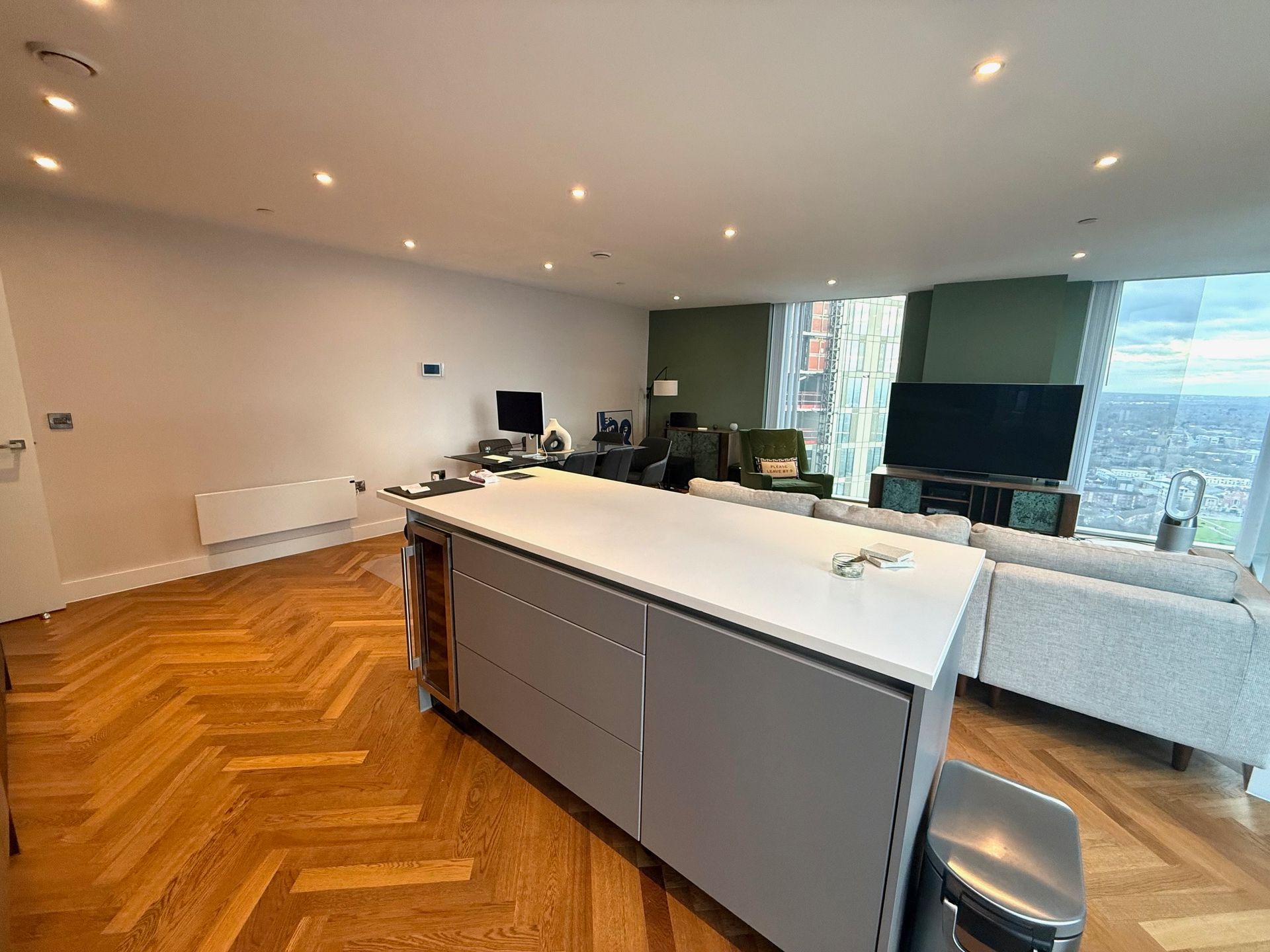 Modern living room with kitchen island, hardwood floors, and city views.