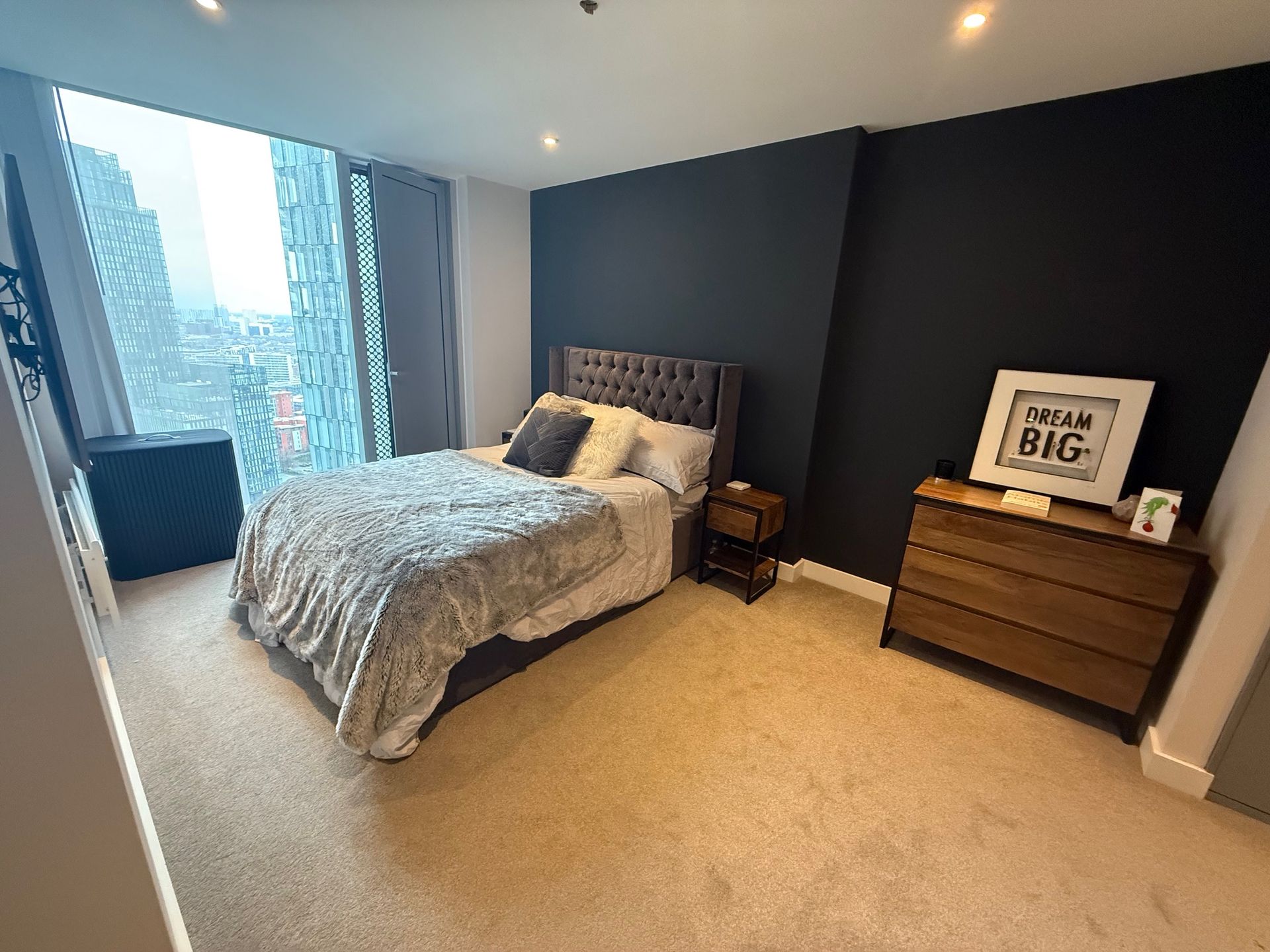 Bedroom with bed, dark accent wall, city view window, and a dresser.