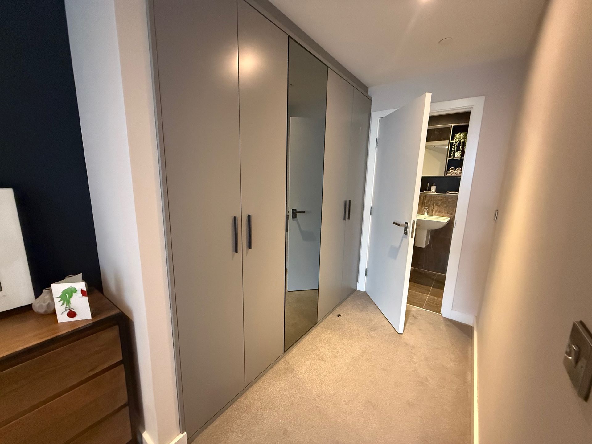 Bedroom with gray closet doors, partially open door to bathroom with sink, tan carpet.