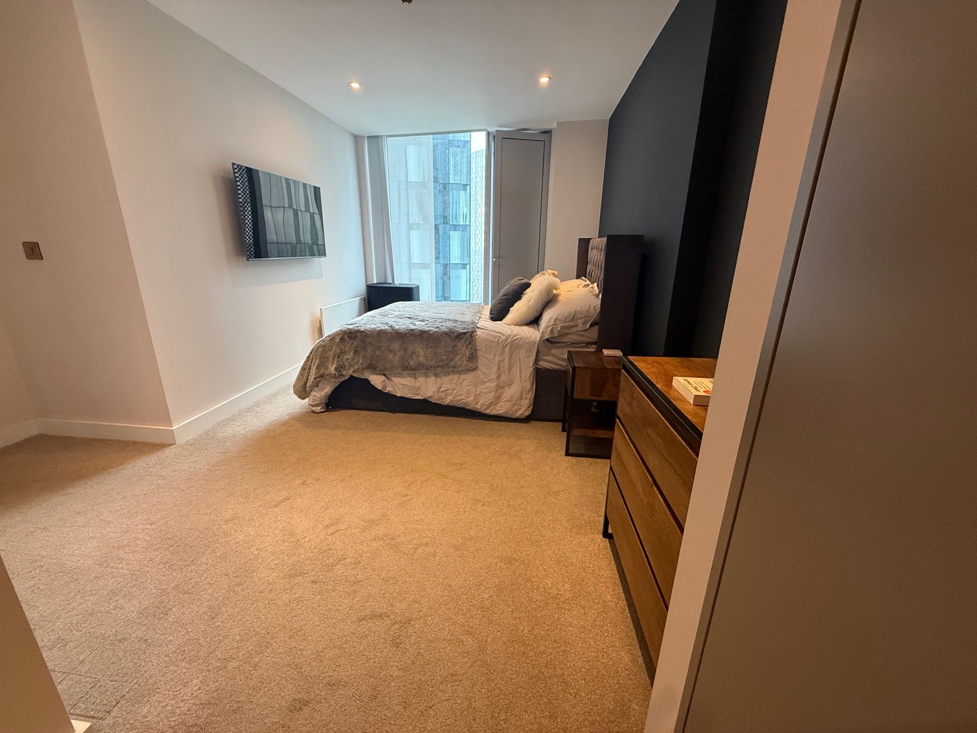 Bedroom with bed, dresser, TV on wall, and windows.