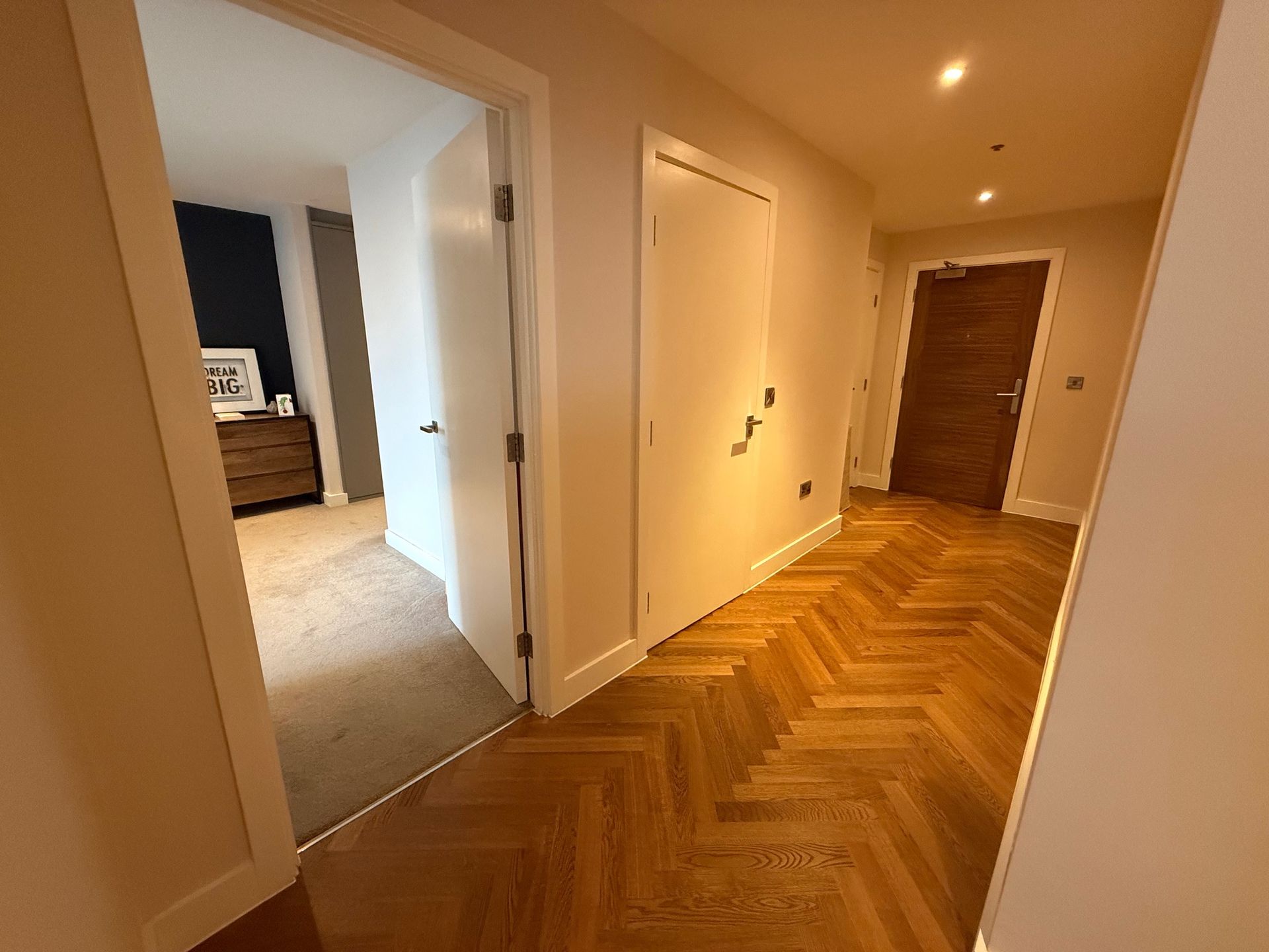 Hallway with parquet flooring, white doors, and a glimpse of a bedroom.