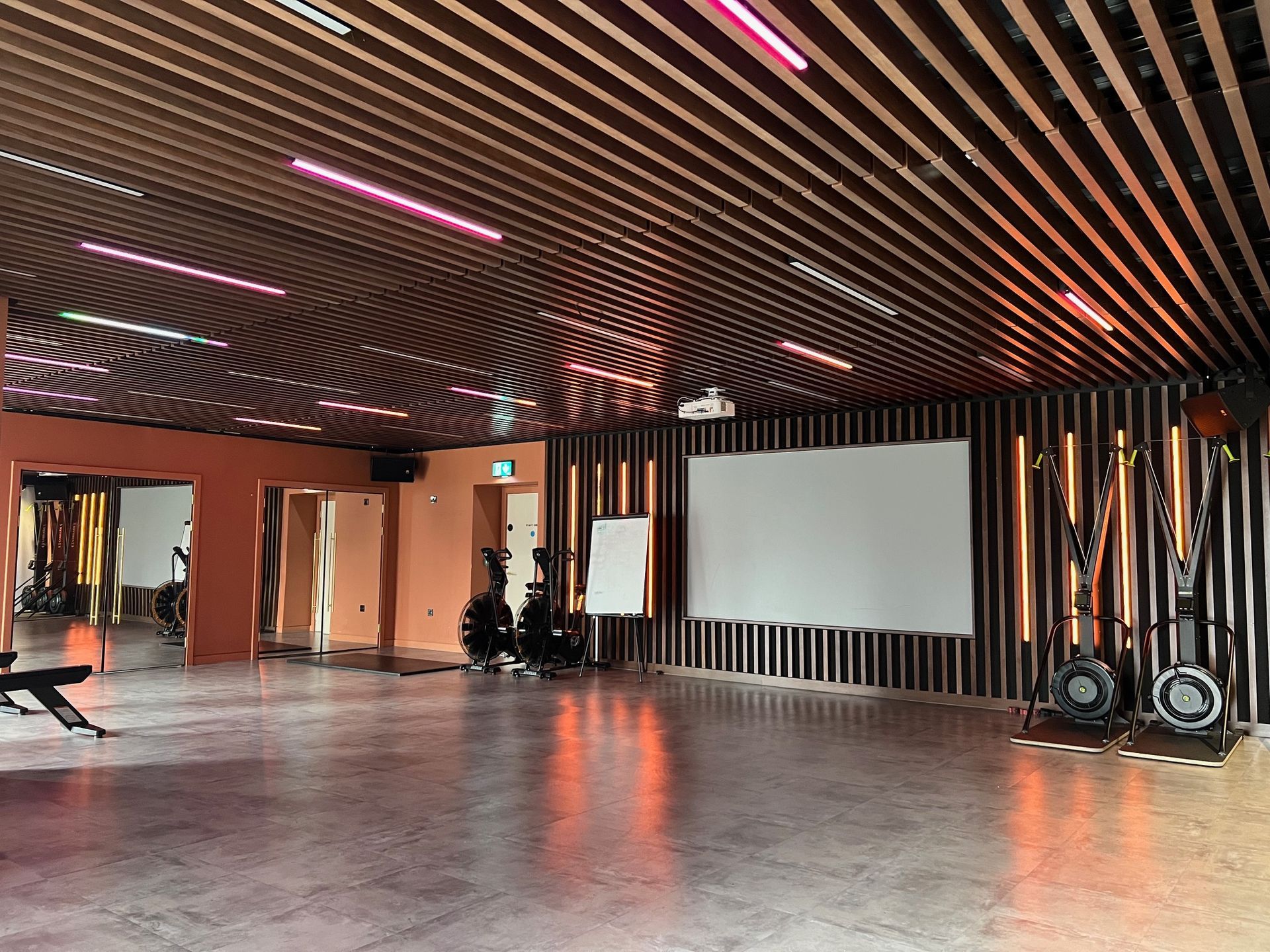 Modern studio with curved wood ceiling, orange walls, projection screen, and exercise equipment.