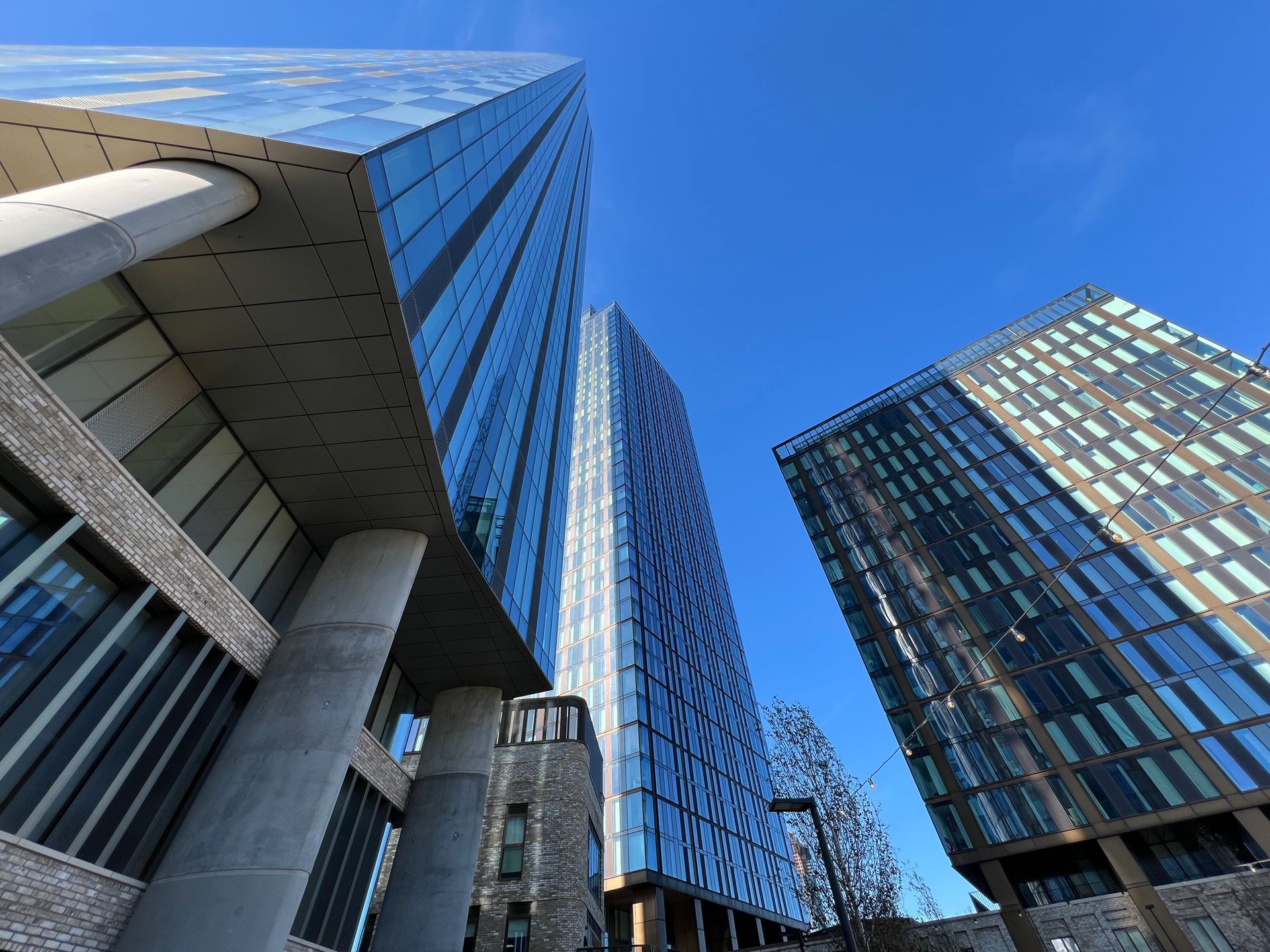 Modern skyscrapers against a bright blue sky, viewed from a low angle. Glass and brick facades.