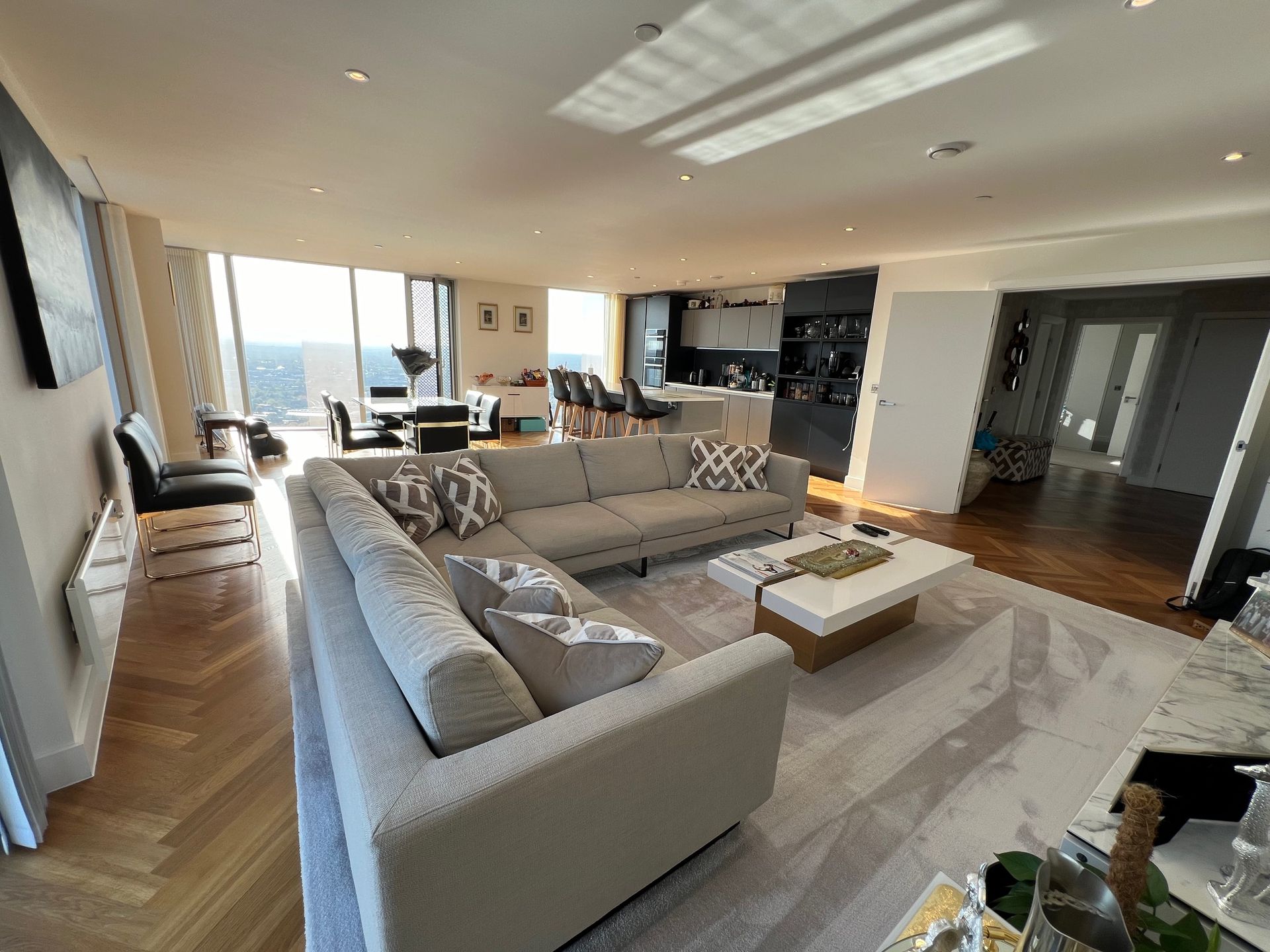 Modern living room with a large gray sectional, hardwood floors, and city views.