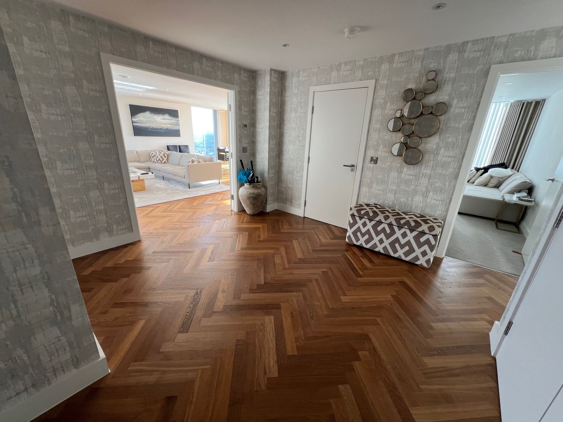Wooden floor hallway with doorways, neutral wallpaper, and decorative items.