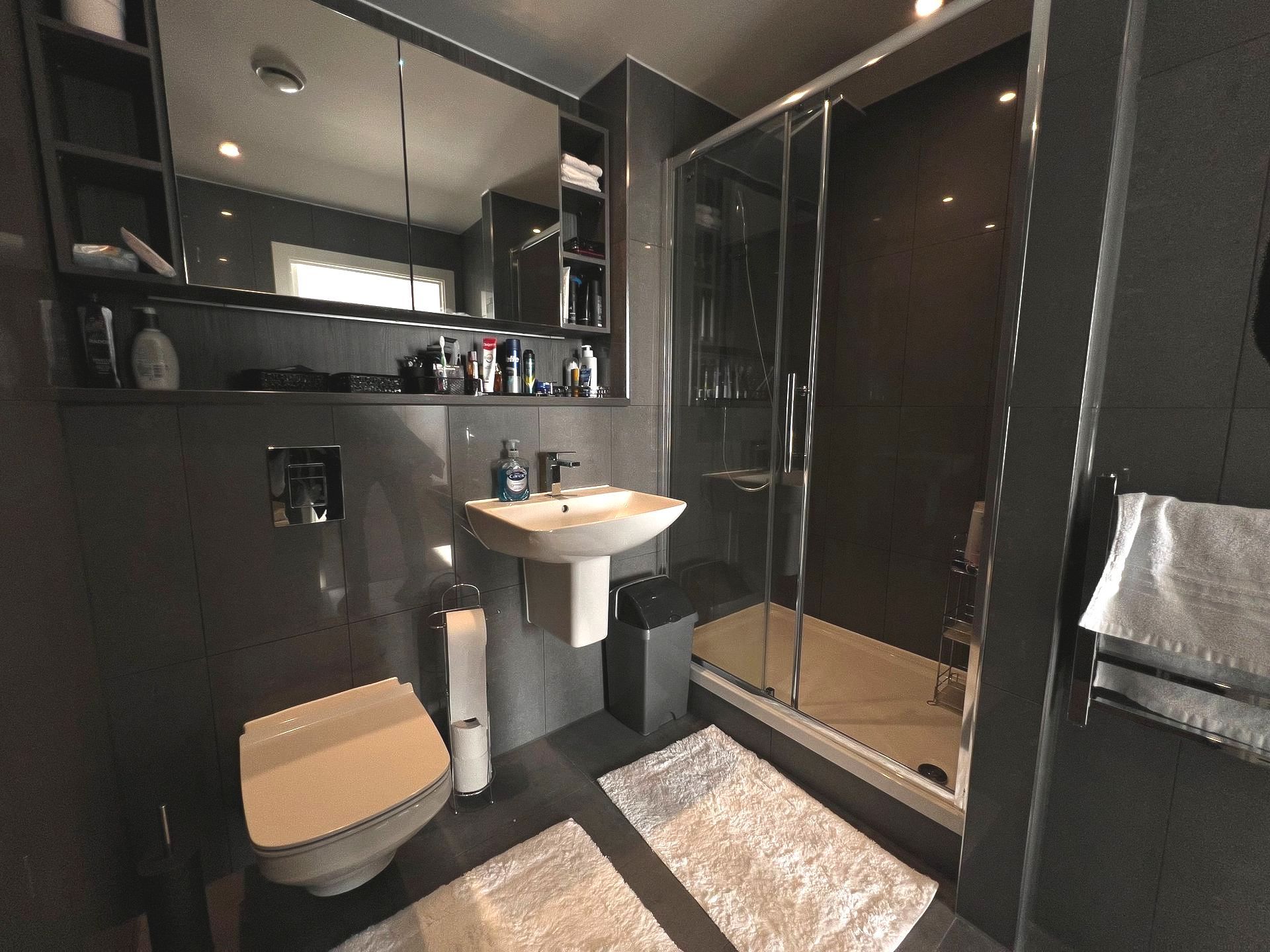 Modern bathroom with dark gray walls, glass shower, toilet, sink, and mirror.