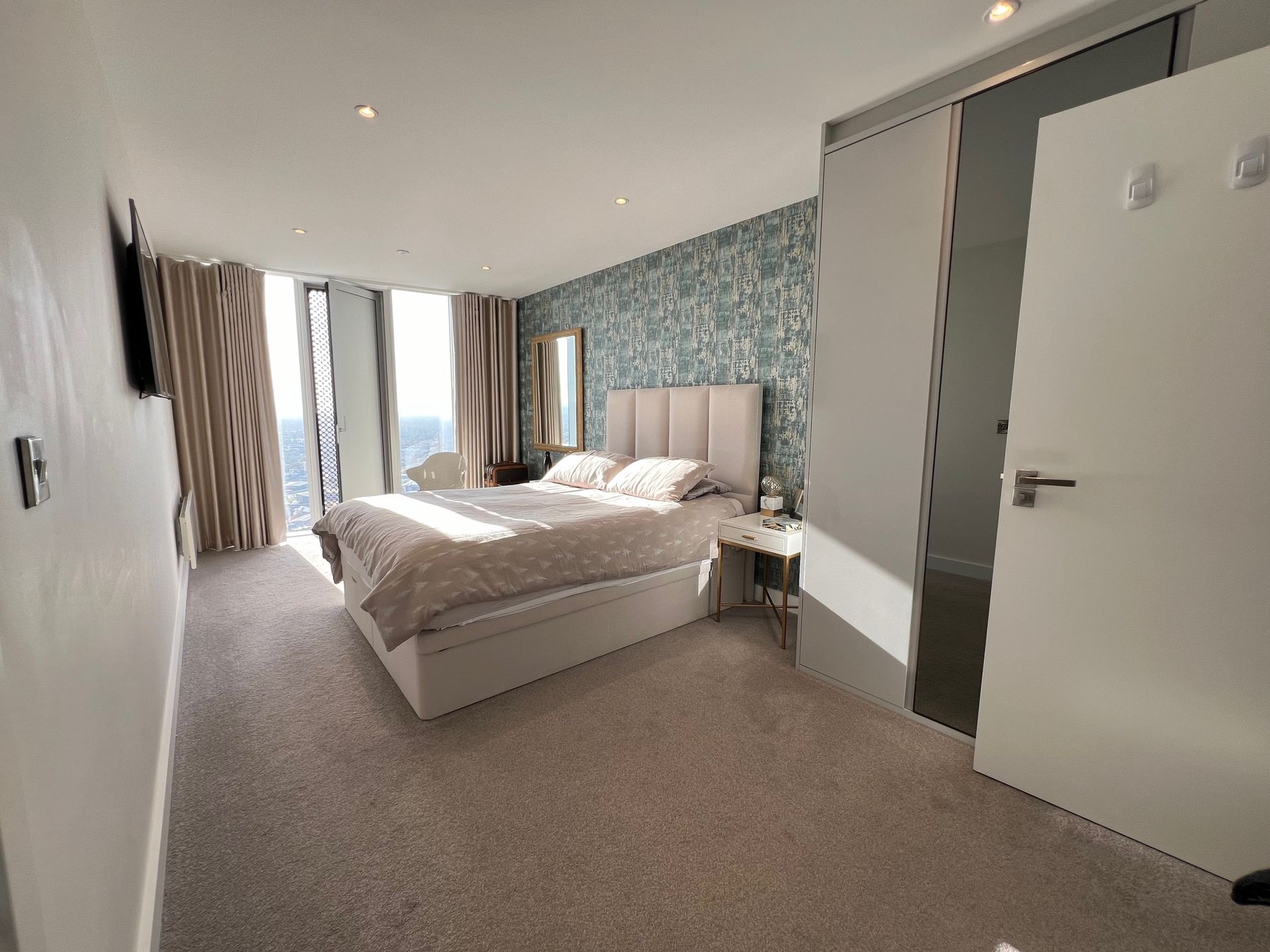 Bedroom with bed, patterned wallpaper, large windows, and neutral color scheme.