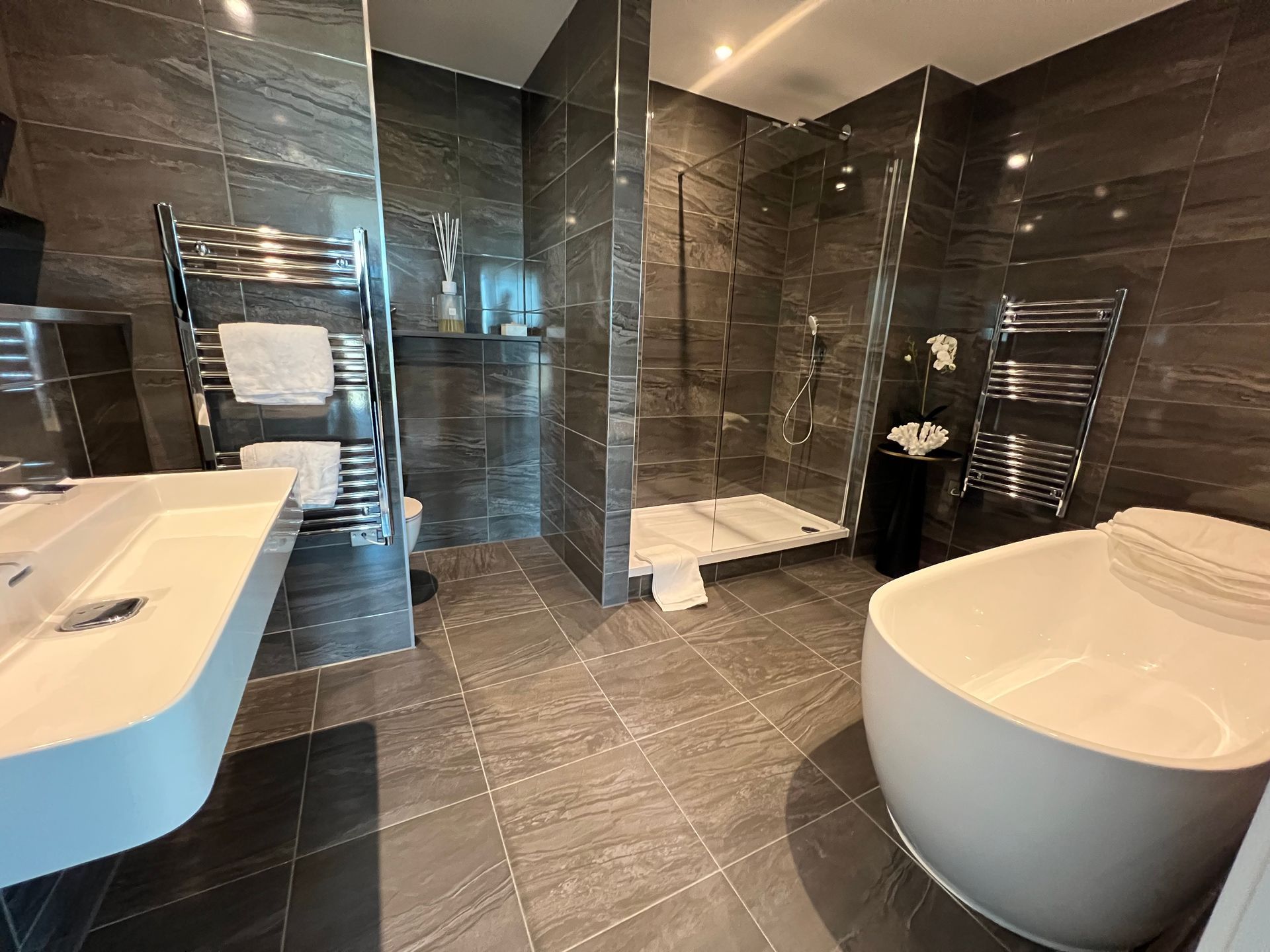 Modern bathroom with dark grey tile, shower, tub, and heated towel racks.