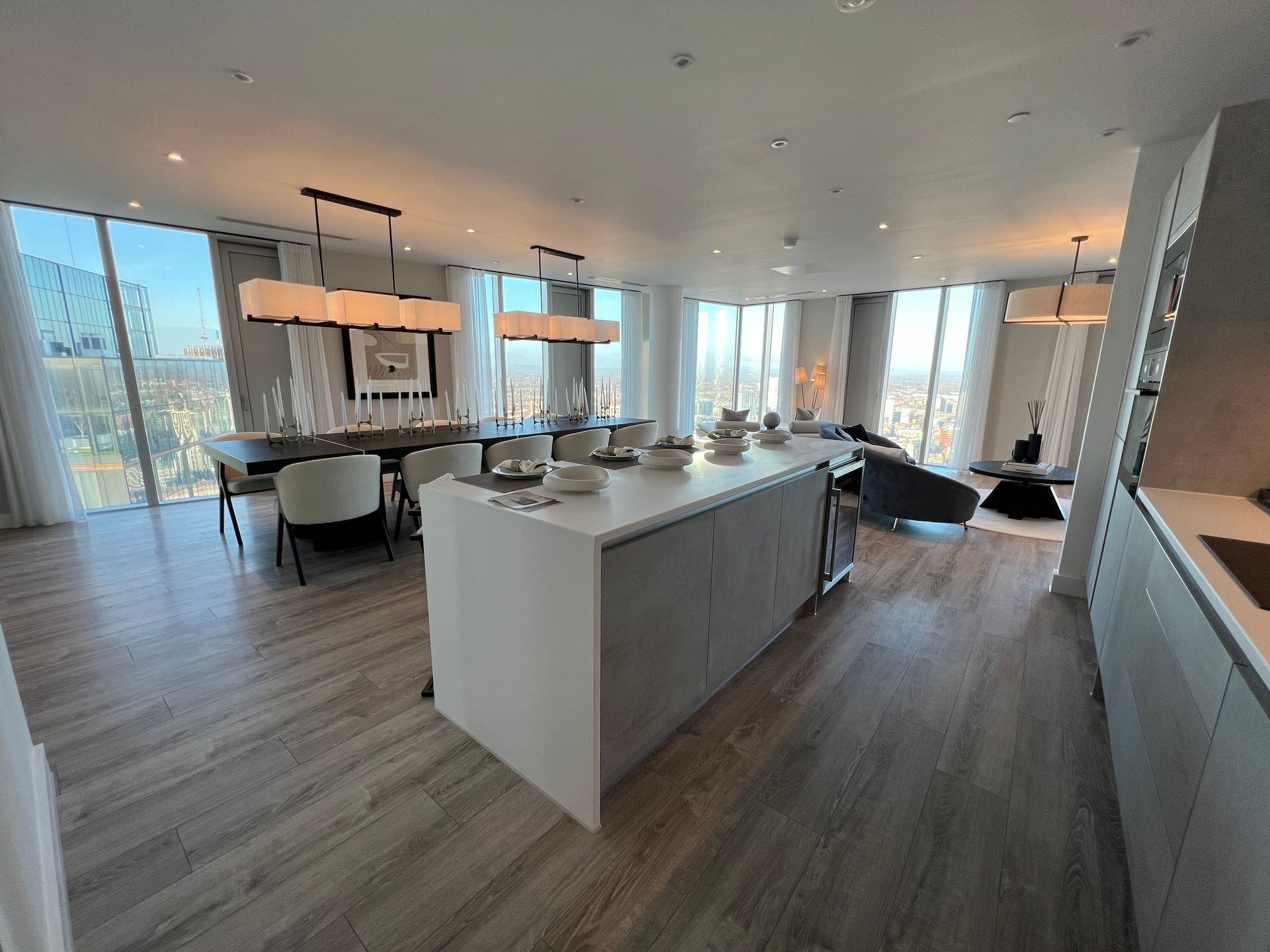 Modern, open-concept kitchen and dining area with city views. Wooden floors, large island, and contemporary furniture.