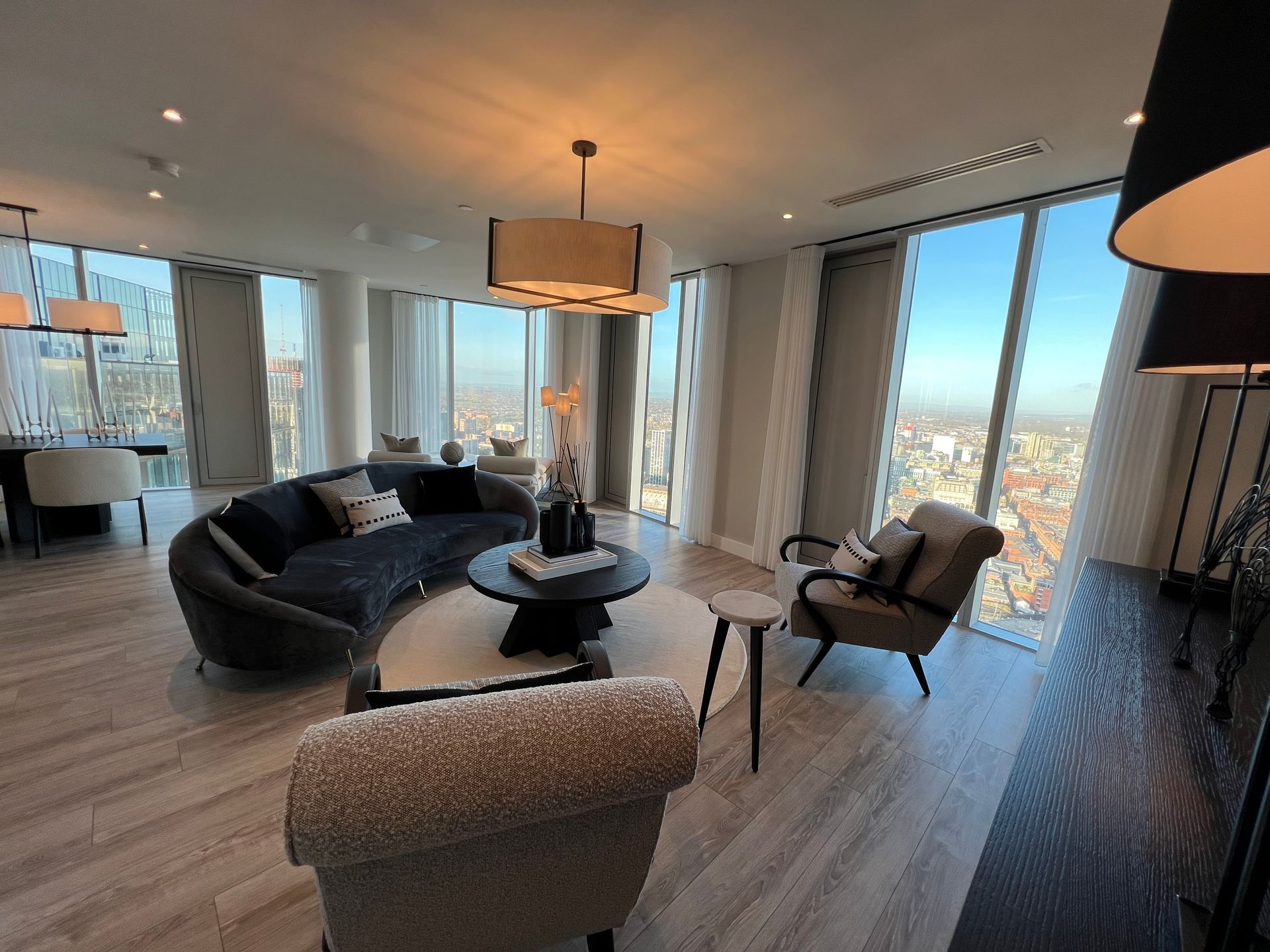Modern living room with curved sofa, large windows, and city view.