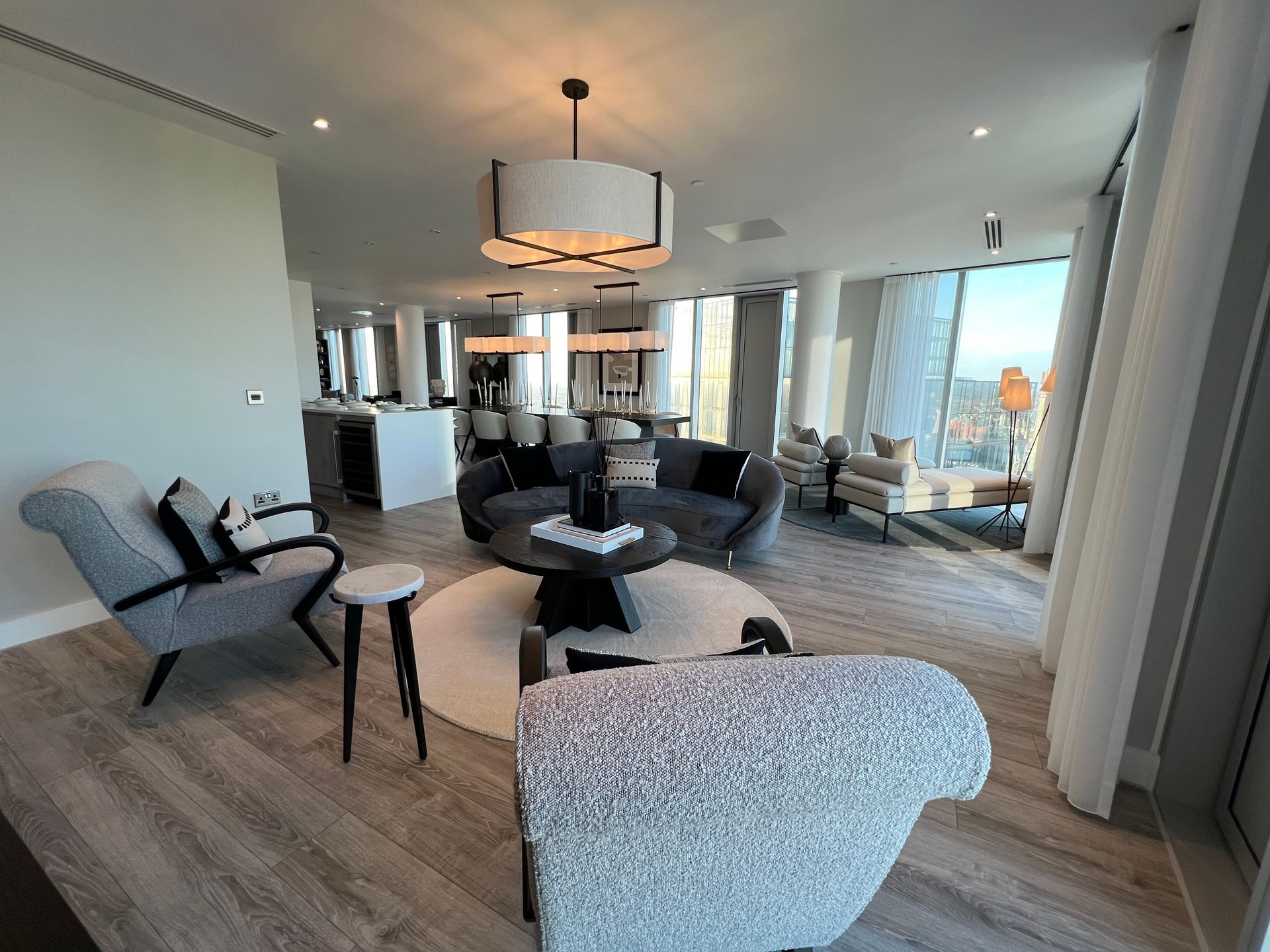 Modern living room with neutral colors, round rug, and large windows offering a city view.