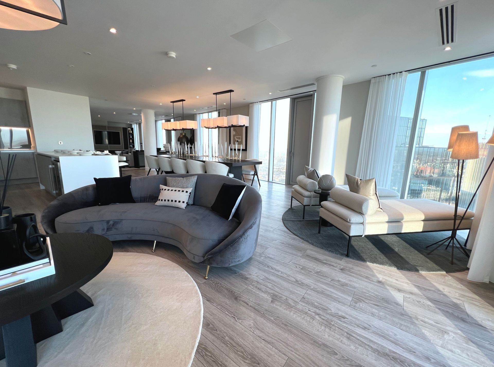 Spacious modern living room with gray curved sofa, dining table, and large windows with city views.