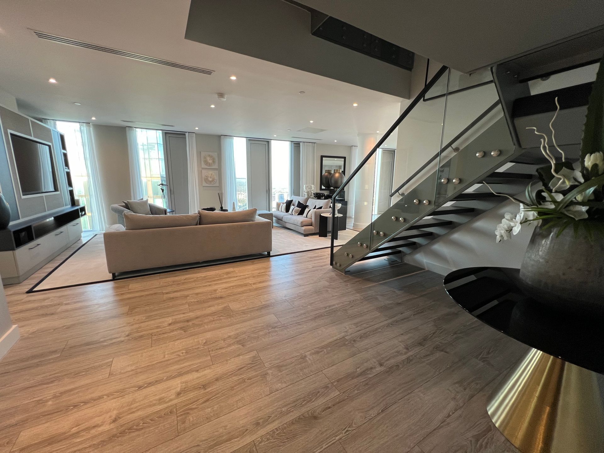 Spacious modern living room with wood floors, neutral furniture, and a staircase.