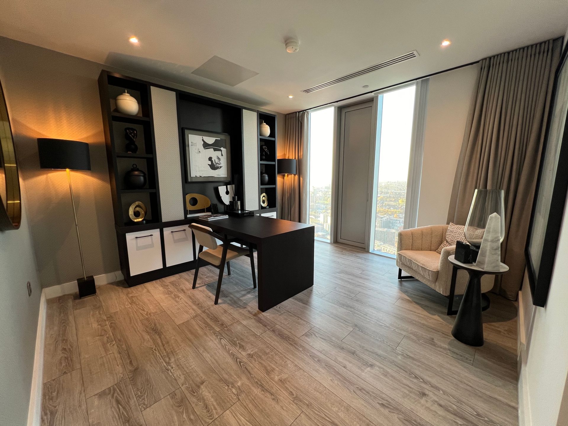 Modern office with black desk, chair, shelves, and armchair. Large windows with city view.