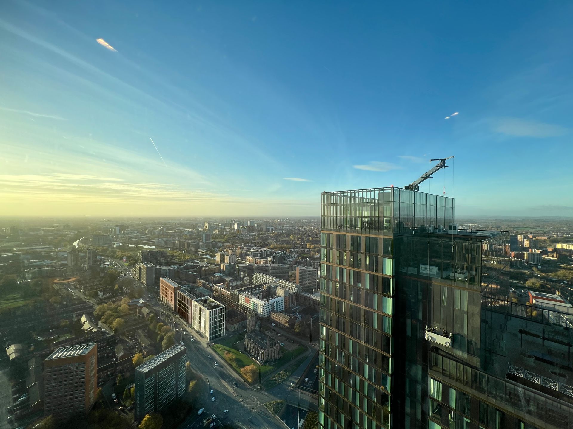 City skyline view from a skyscraper, including the building's edge with a crane and clear blue sky.