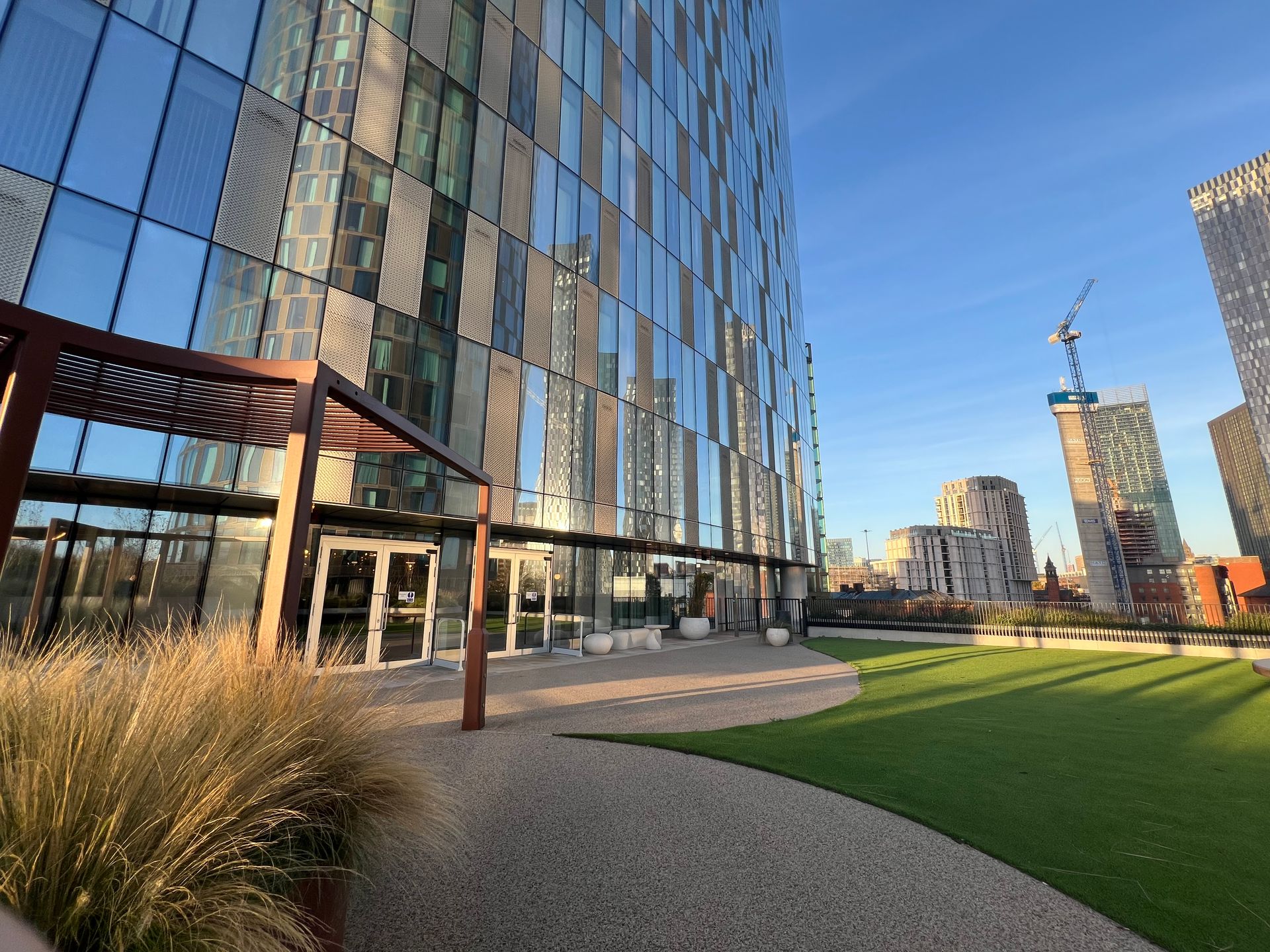 Modern glass building exterior with green space and city views under a blue sky.