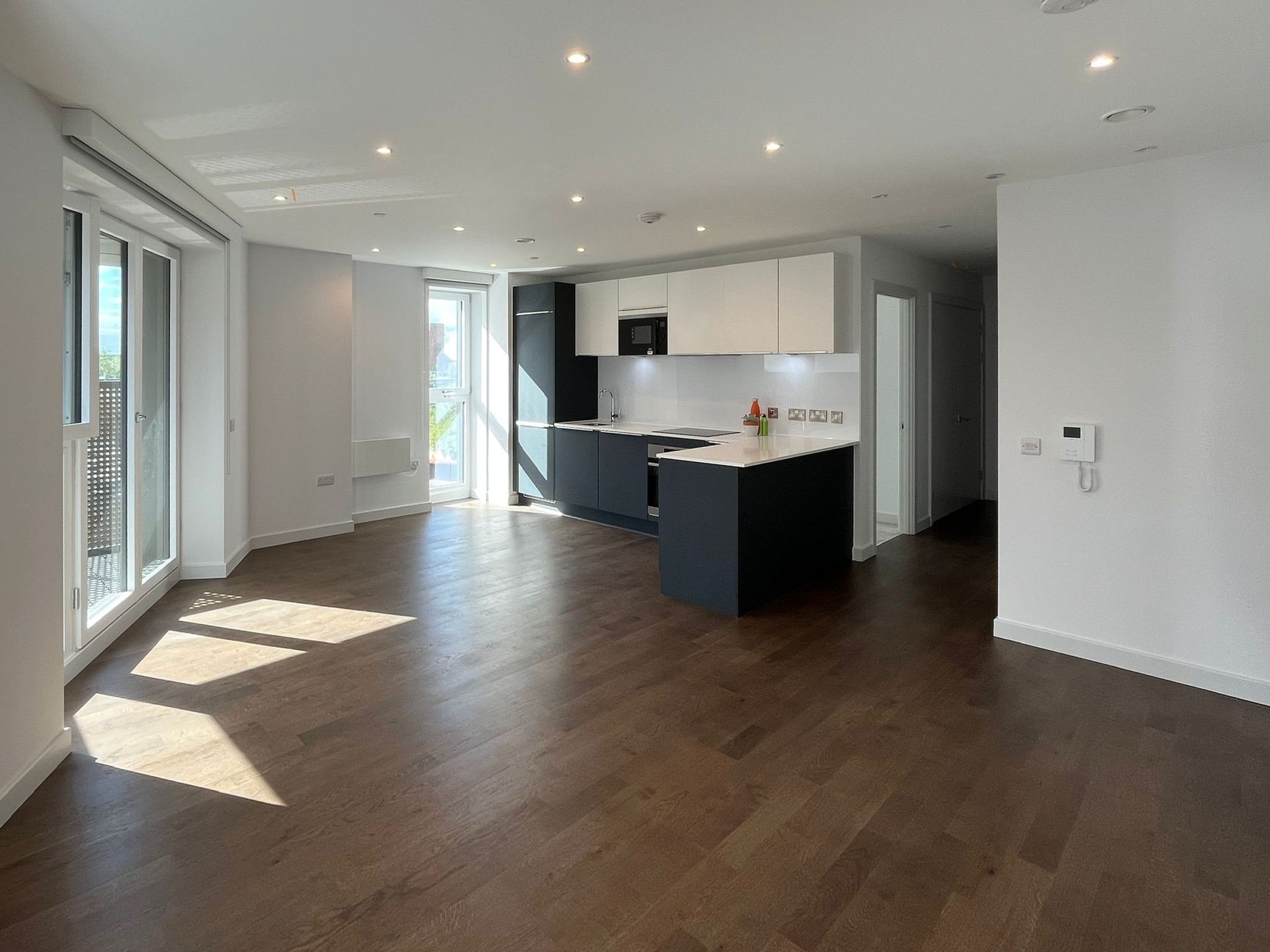 Open-plan modern apartment with dark wood floors, white walls, and a grey and white kitchen.