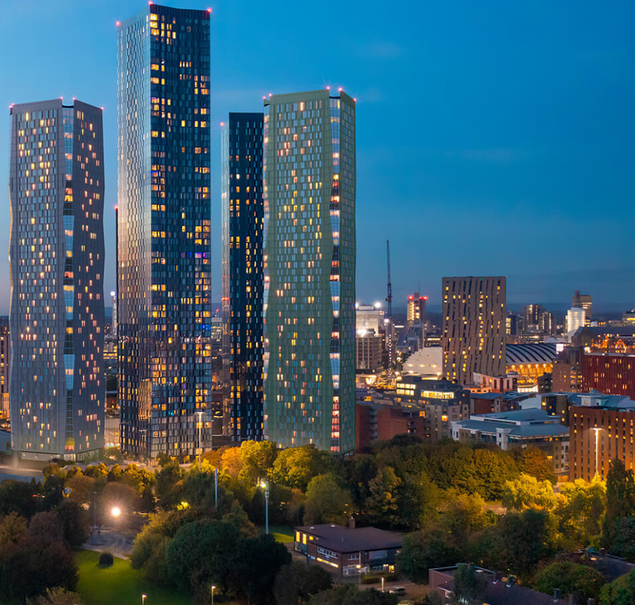 Skyscrapers illuminate a cityscape at dusk. Trees and other buildings fill the foreground and middle ground.