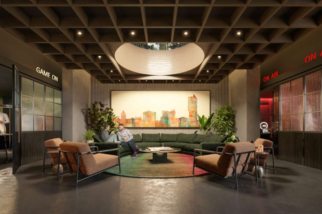 Lobby with seating around a rug; a person sits on a green sofa, artwork on the wall, and overhead lighting.