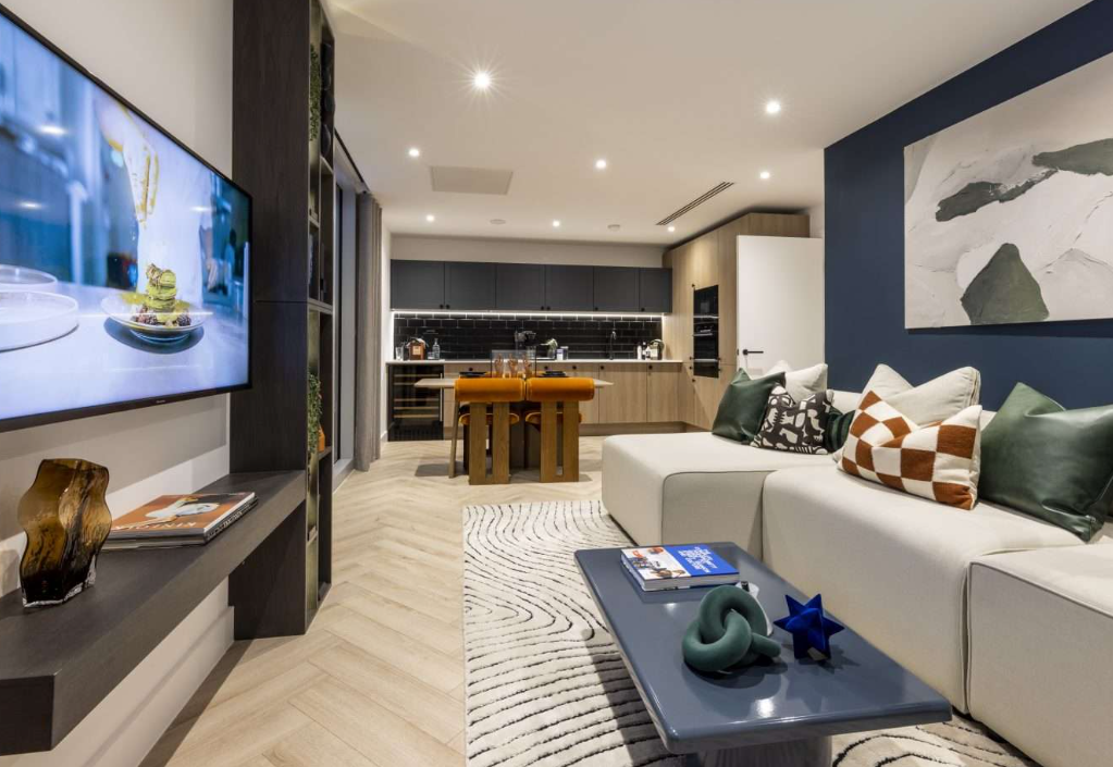 Modern living room with kitchen in background; white sofa, blue accent wall, wooden floors.