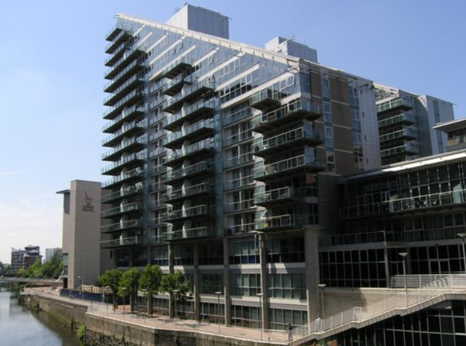 Modern glass and steel apartment building with balconies along a canal.