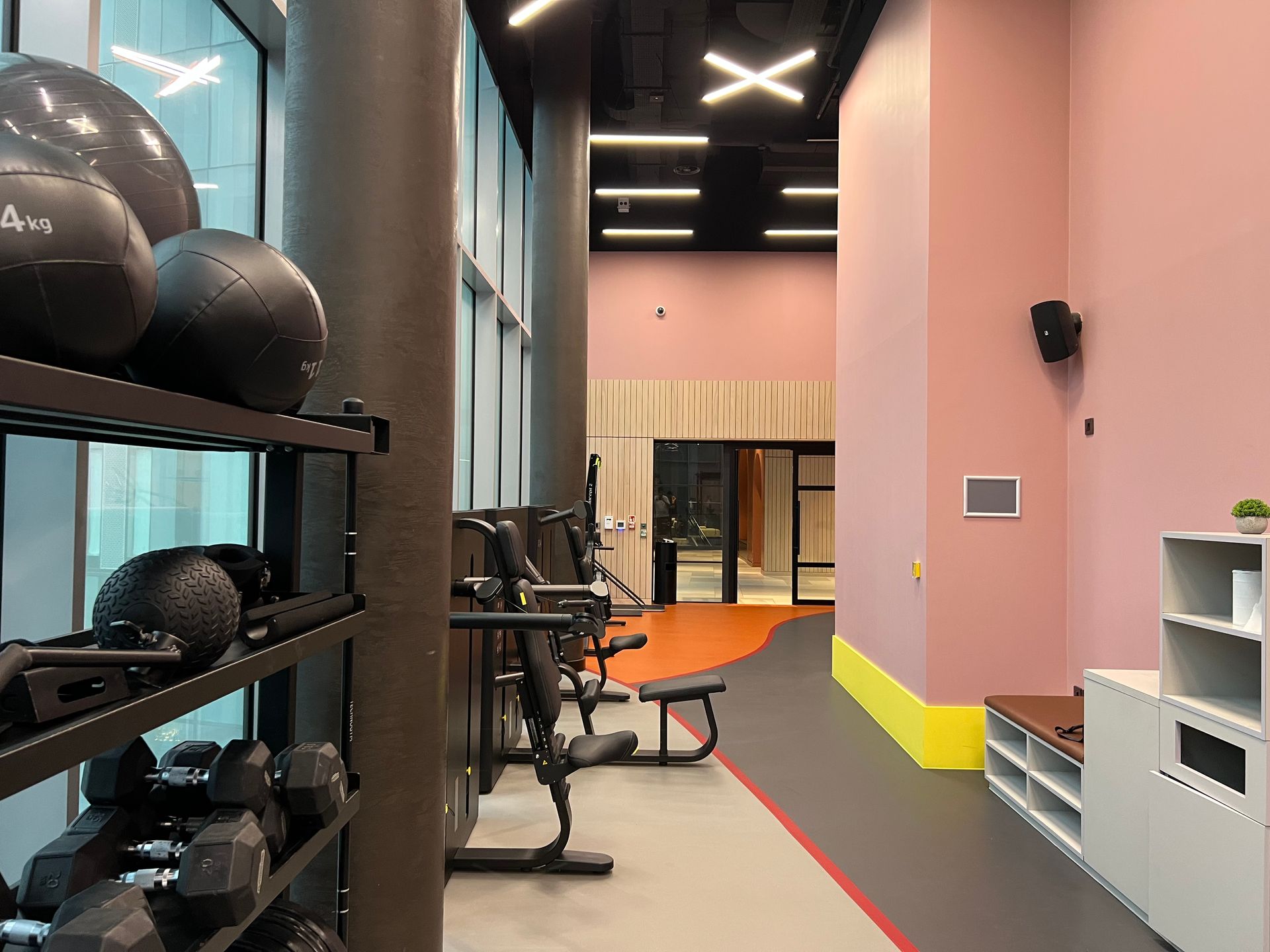 Gym interior with weights, exercise machines, and a hallway with pink walls.